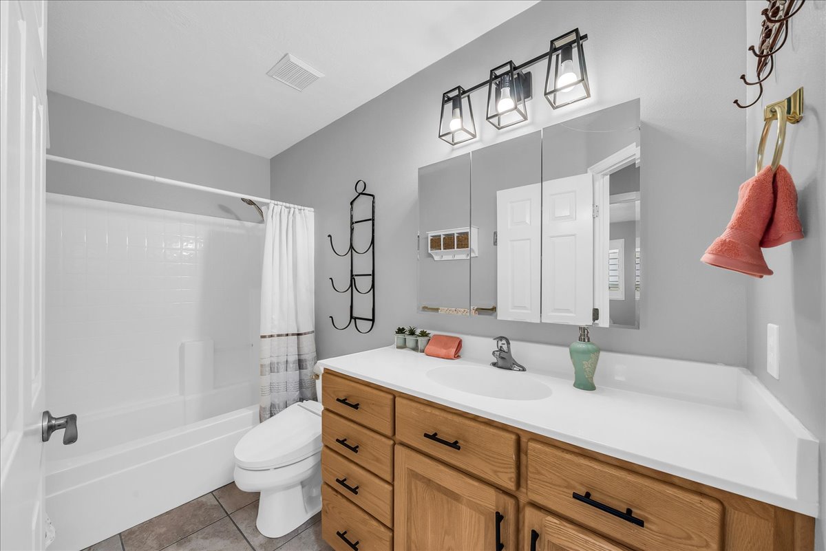 Bathroom featuring a wood-finish vanity with a white countertop and integrated sink, a three-mirror medicine cabinet, and overhead lighting with metal cage fixtures