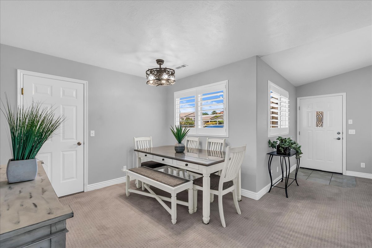 Carpeted dining area featuring a decorative chandelier, white plantation shutters, and a tiled entryway