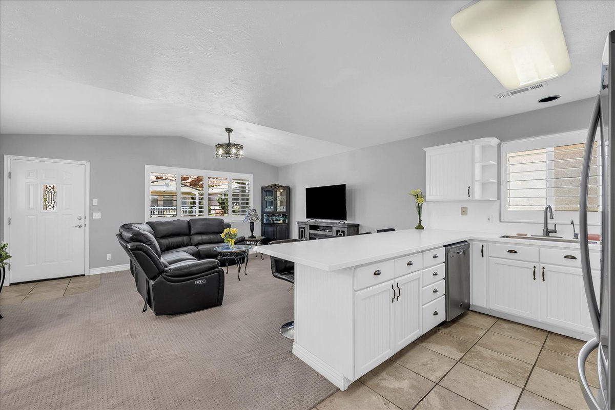 Open-concept living area featuring a kitchen island with white cabinetry, stainless steel dishwasher, and a sink with a gooseneck faucet