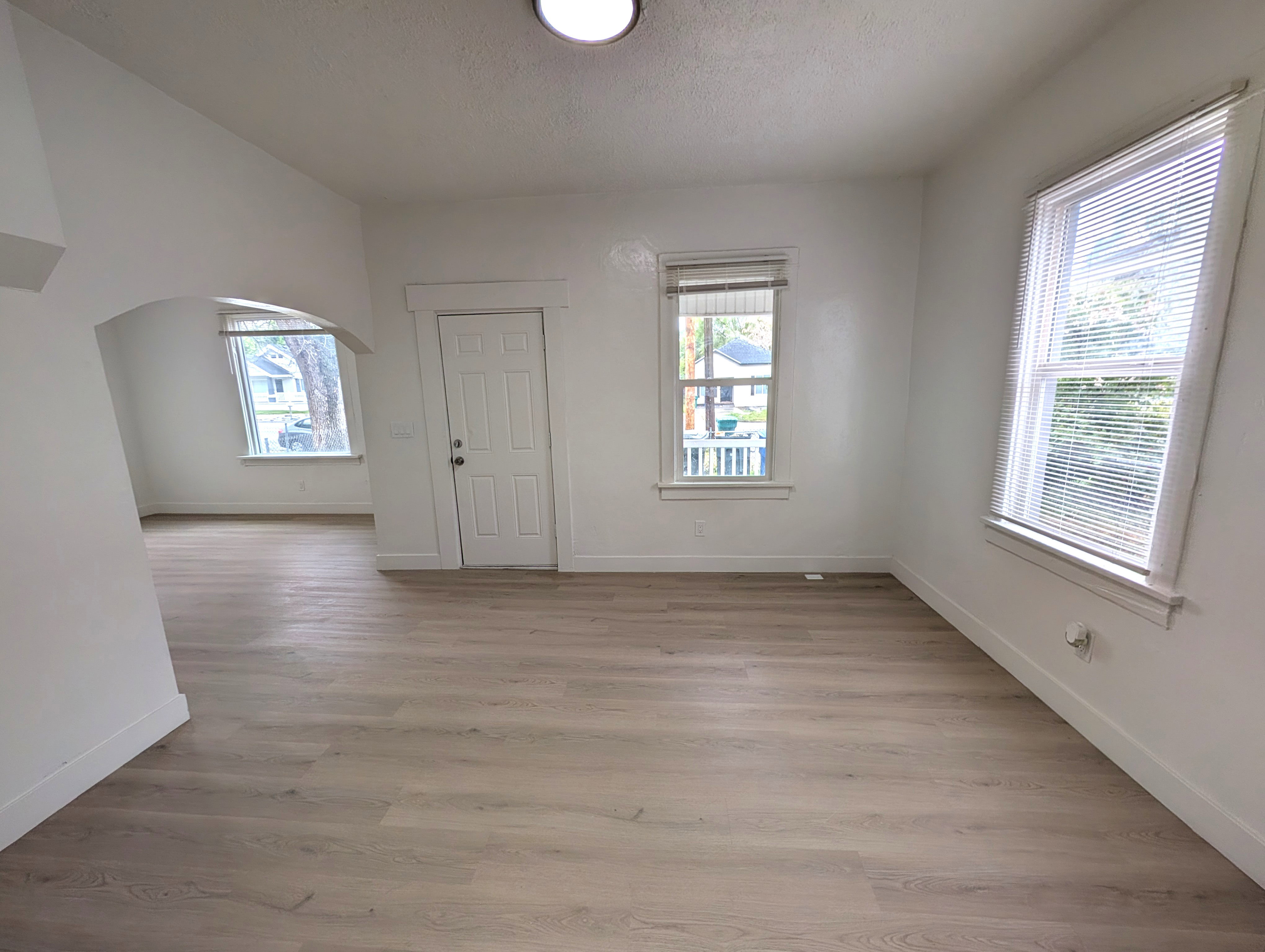 Spacious interior featuring light wood-finish flooring, white painted walls, and multiple windows with blinds