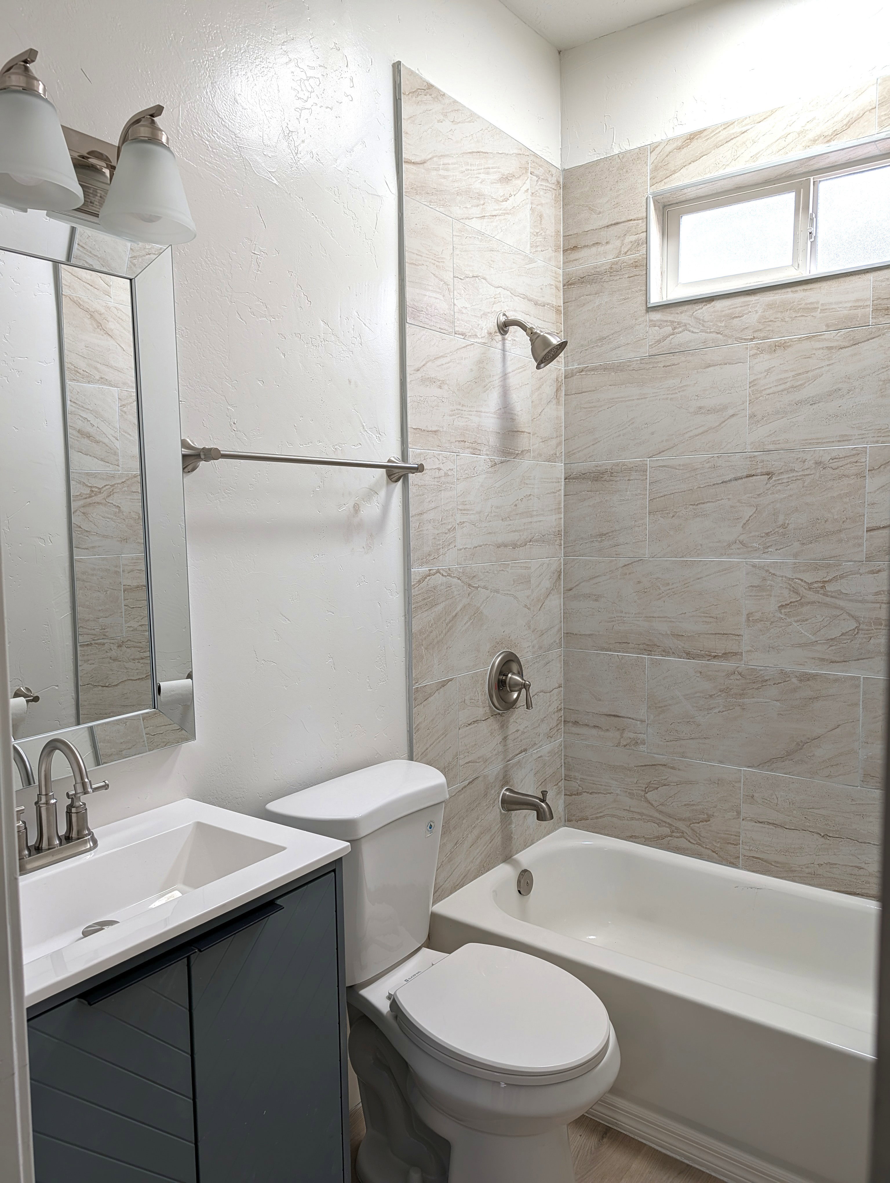 Full bathroom featuring a rectangular vanity sink with a gray cabinet, a toilet, and a bathtub with a tiled surround