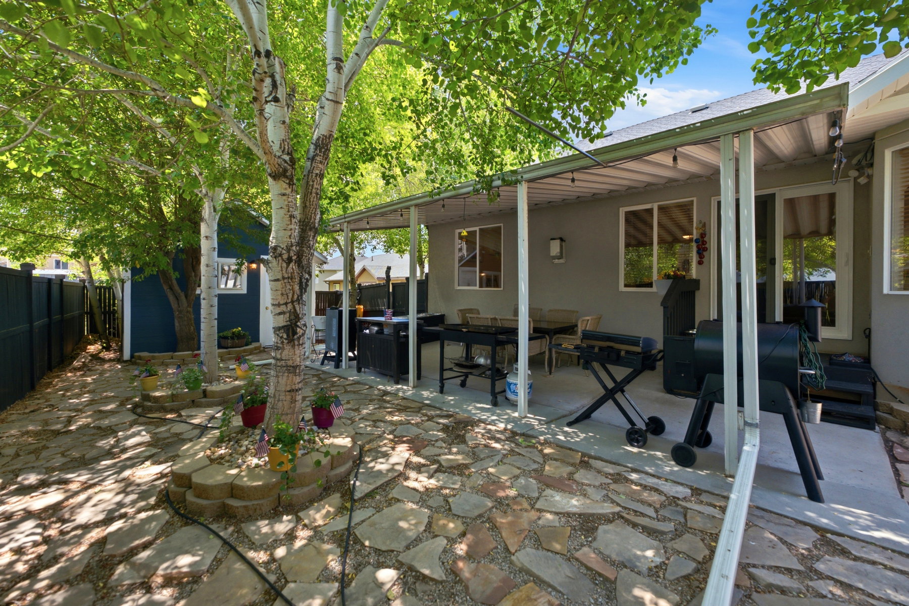 Covered patio with a concrete slab, stone paver ground covering, mature trees, and a privacy fence