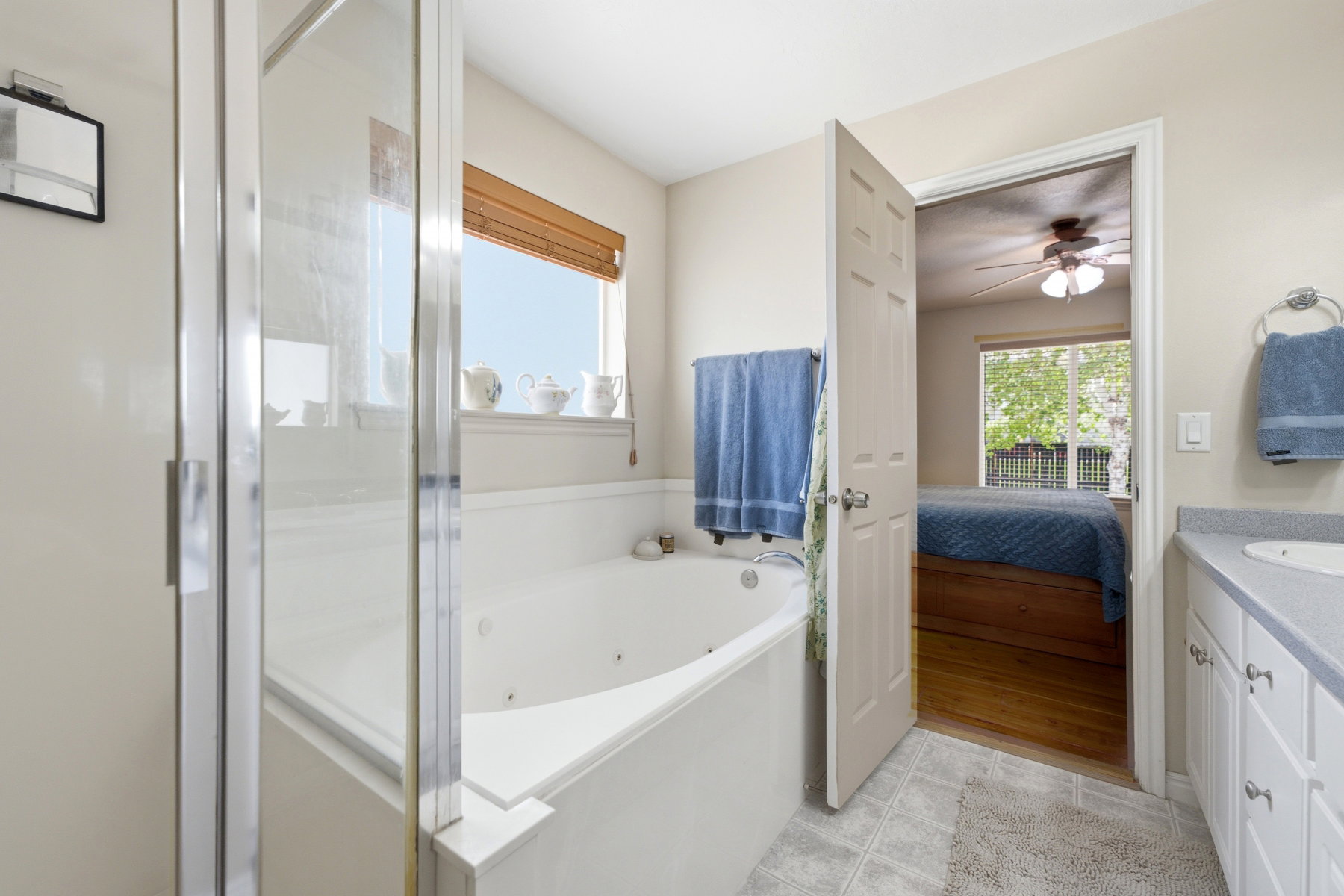 Primary suite bathroom with a glass-enclosed shower, built-in soaking tub, a window with a wood-slat blind, and a vanity with a countertop and under-sink cabinetry