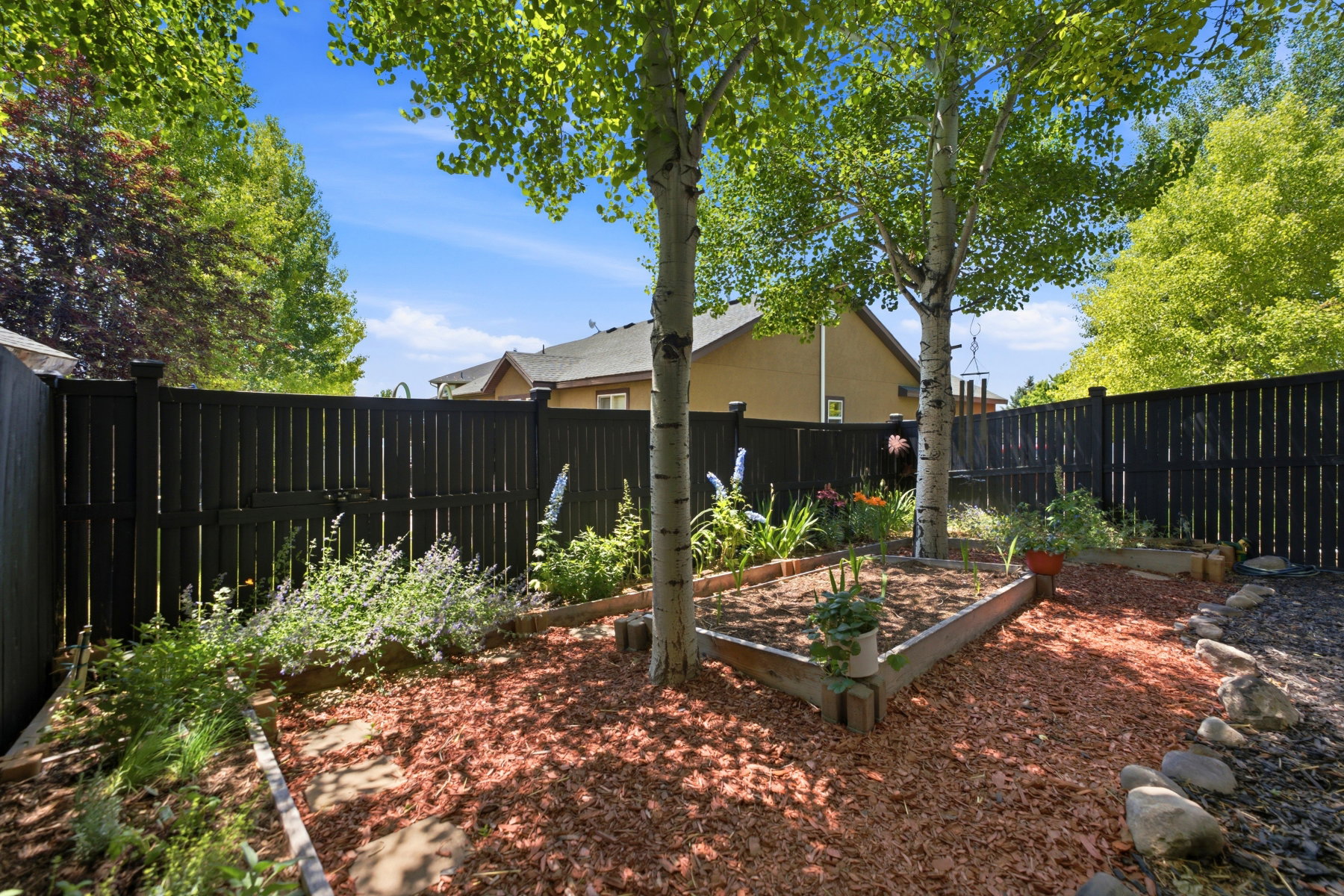 Fenced yard featuring a wooden privacy fence, mature trees, wood-edged garden beds, and ground cover
