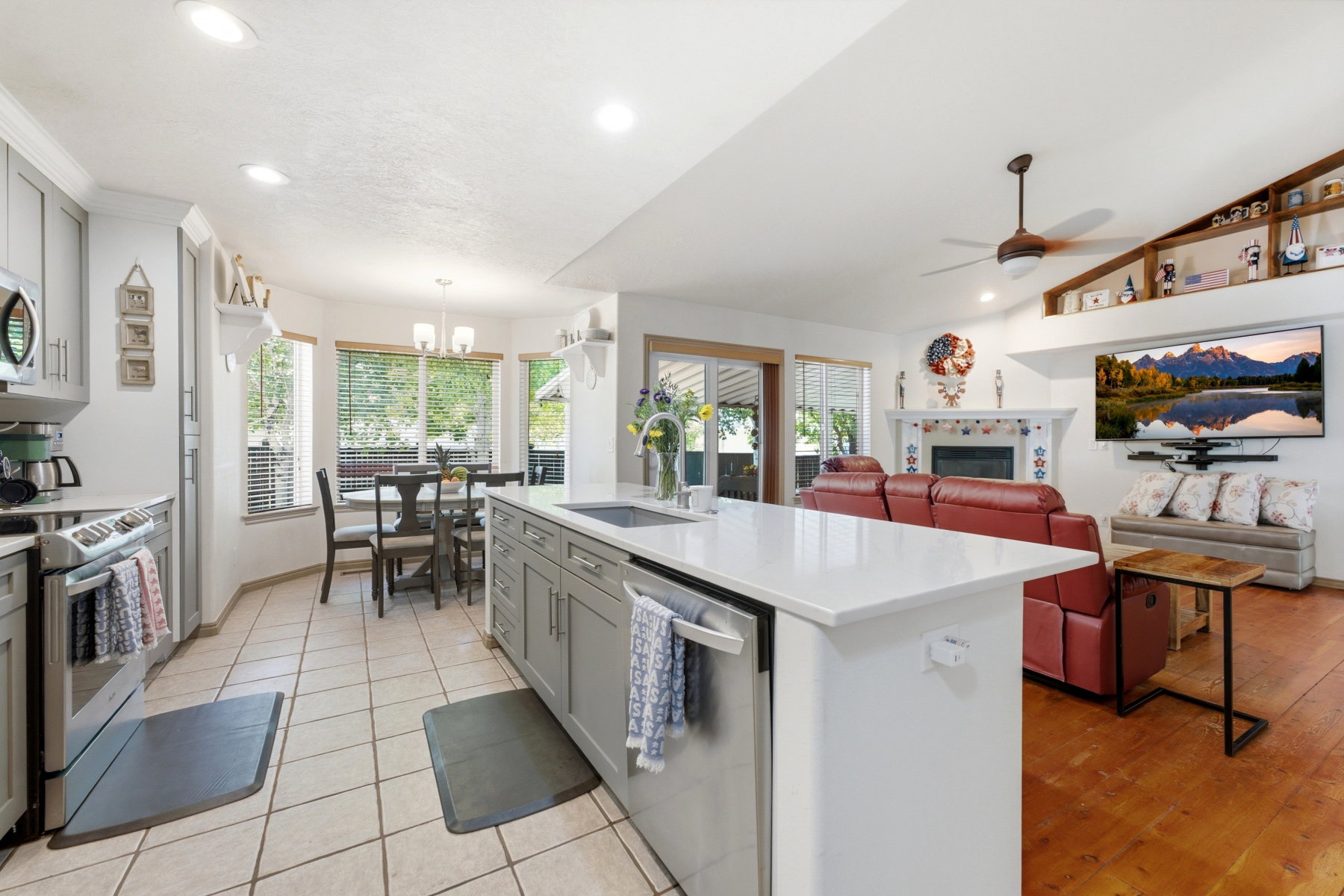 Spacious open-concept living area featuring a kitchen island with sink, white countertops, recessed lighting, a built-in fireplace, and a vaulted ceiling with a fan