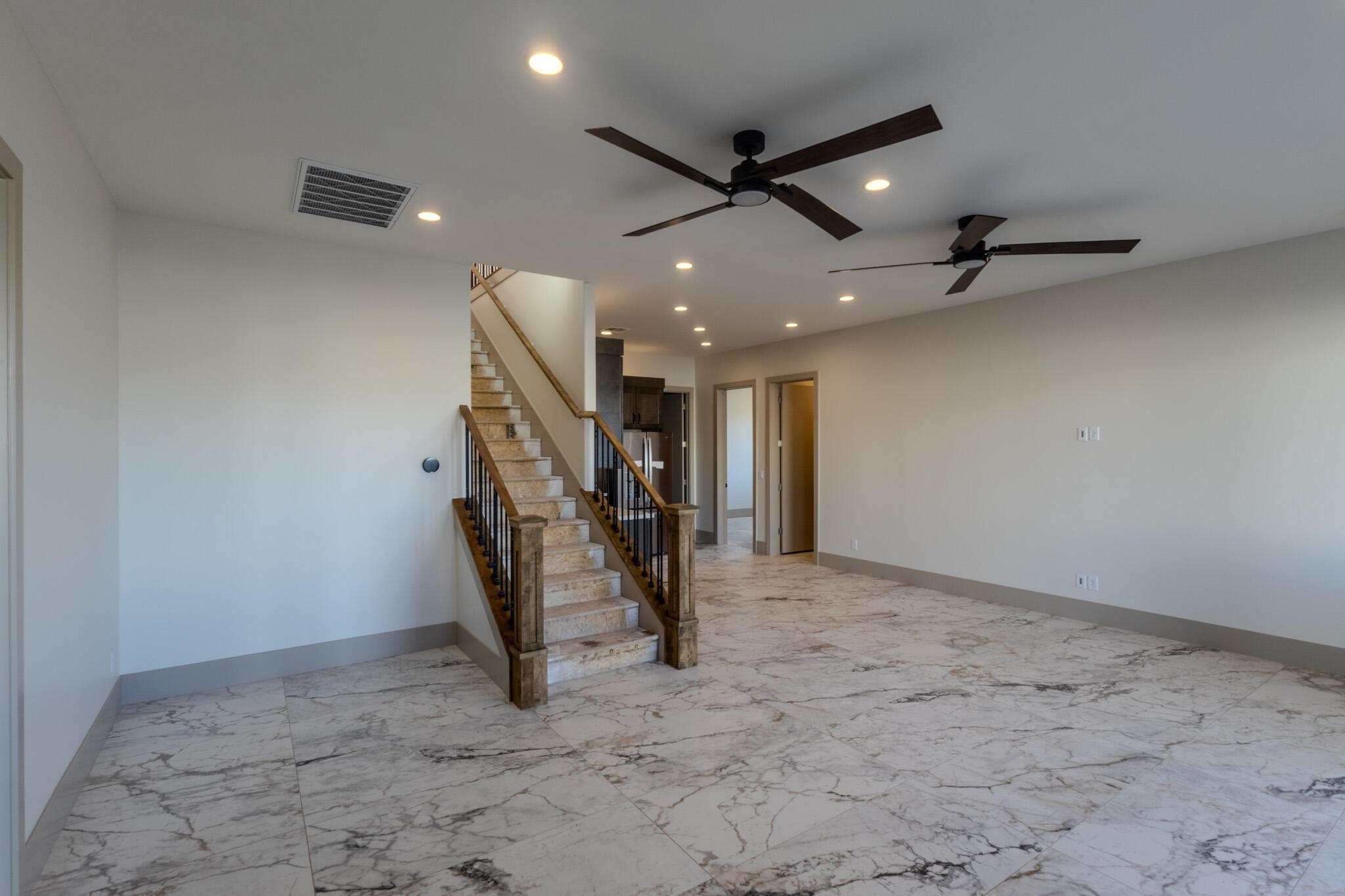 Spacious interior featuring large format marble-look tile flooring, a staircase with wood newel posts and black iron balusters, and a ceiling with recessed lighting and two ceiling fans