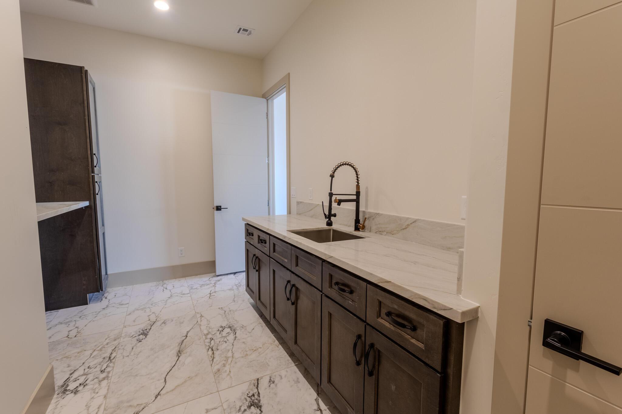 Spacious utility area featuring a dark wood-finish vanity with a stainless steel sink, a modern black faucet, and a light-toned countertop with veining