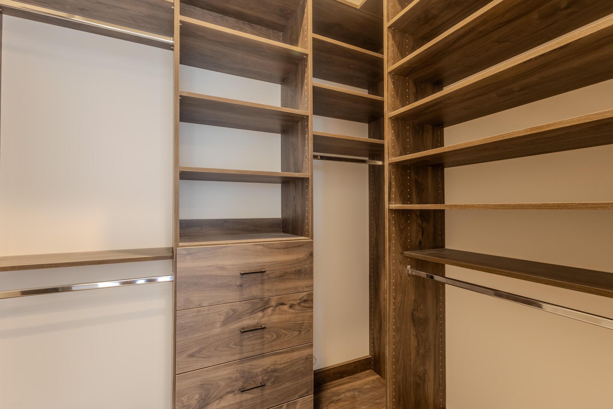 Custom closet system featuring wood-finish shelving, integrated drawer storage with matte black hardware, and multiple chrome hanging rods