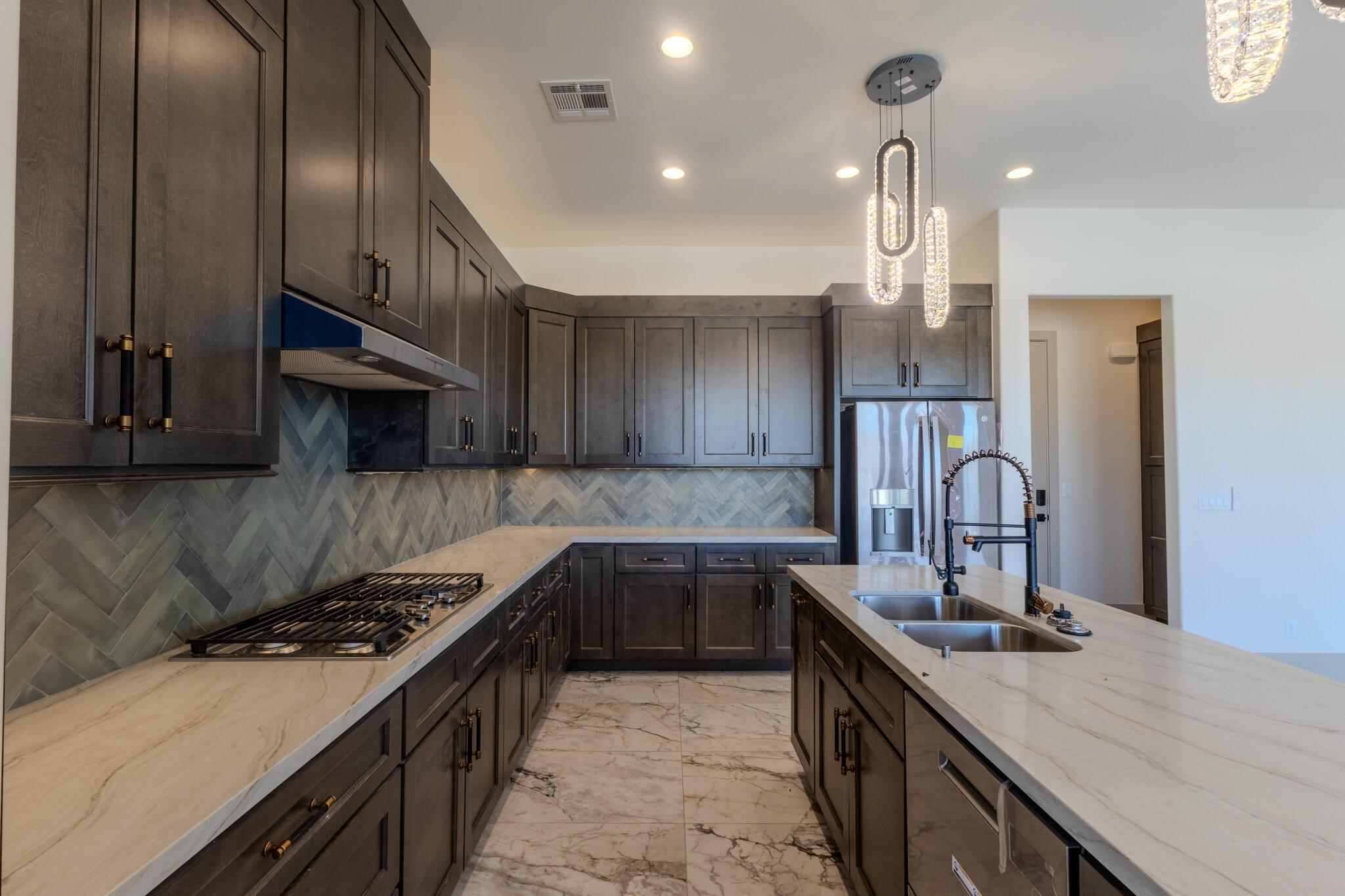 Gourmet kitchen featuring dark wood cabinetry, light-toned countertops, a herringbone tile backsplash, a gas cooktop, and a double basin sink with a gooseneck faucet