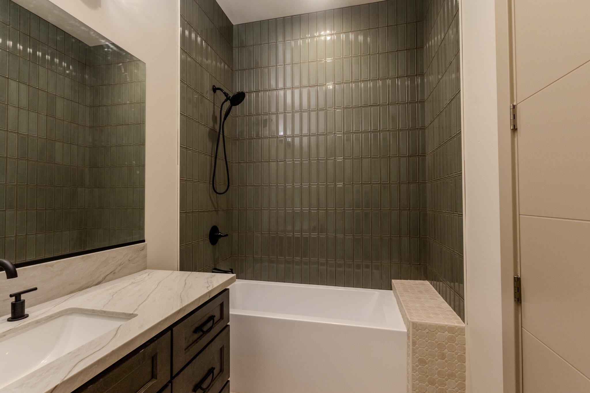 Bathroom featuring a tub/shower combination with vertically stacked subway tile surround, matte black fixtures, a vanity with a rectangular undermount sink, and a stone-finish countertop