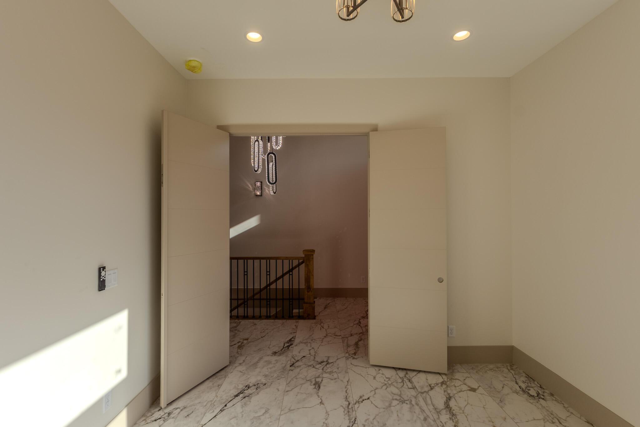 Double pivot doors open to a grand entryway featuring marble flooring and a contemporary chandelier, illuminated by recessed lighting