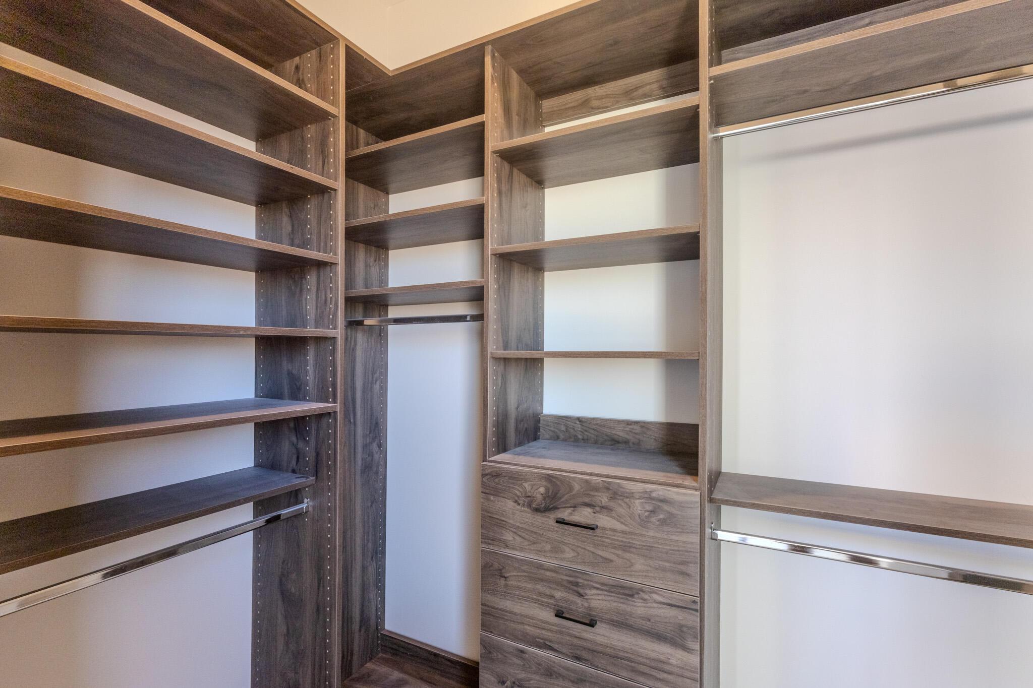 Custom closet system featuring wood-finish shelving, integrated drawers with black hardware, and multiple chrome hanging rods