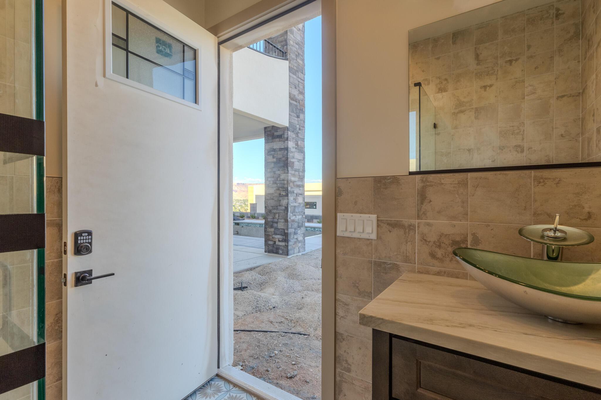 Bathroom entry featuring a vessel sink, stone countertop, wood-finish vanity, and tiled walls