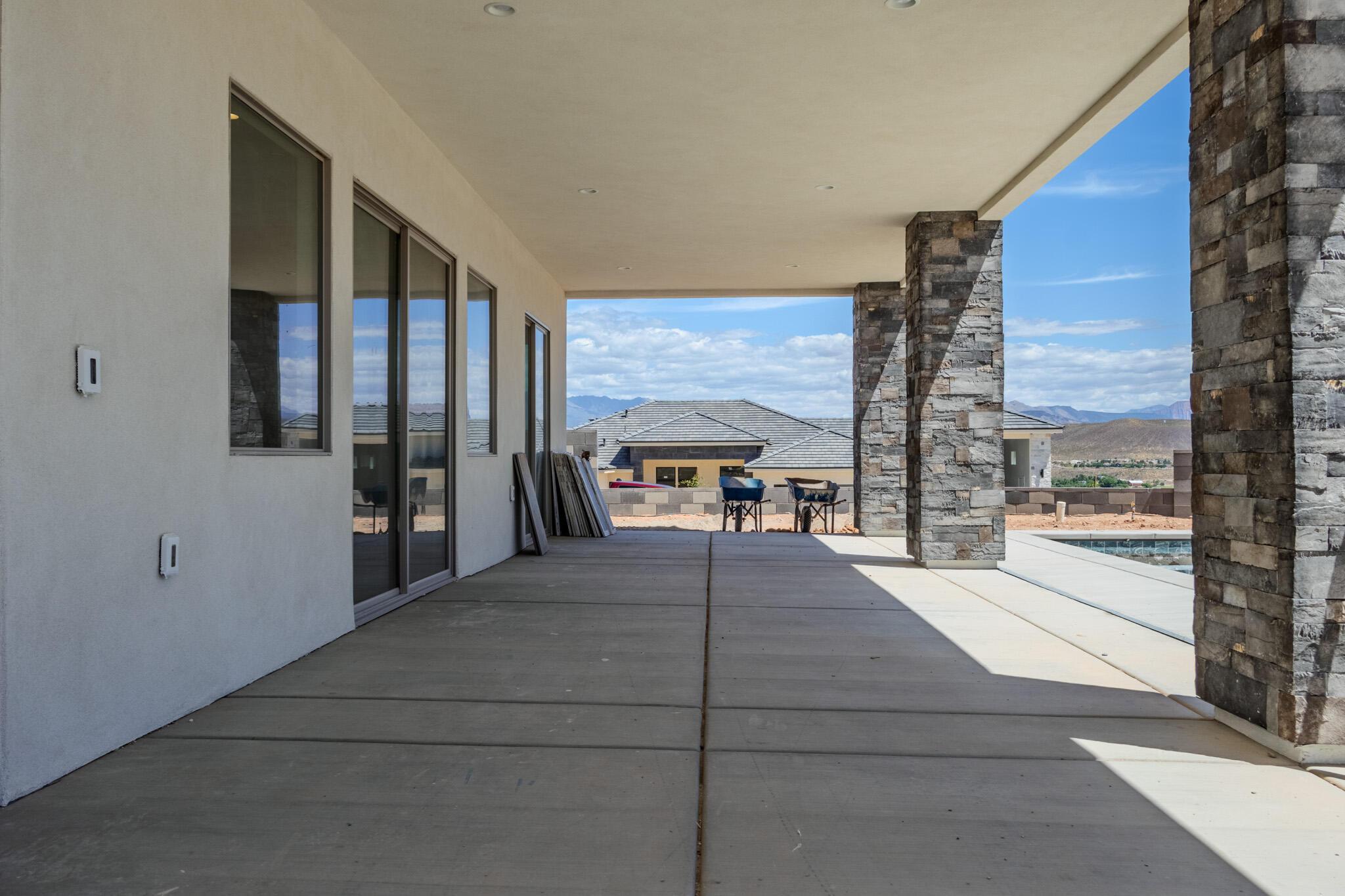 Expansive covered patio featuring a concrete surface, stone-clad support pillars, recessed lighting, and multiple large windows and a sliding glass door