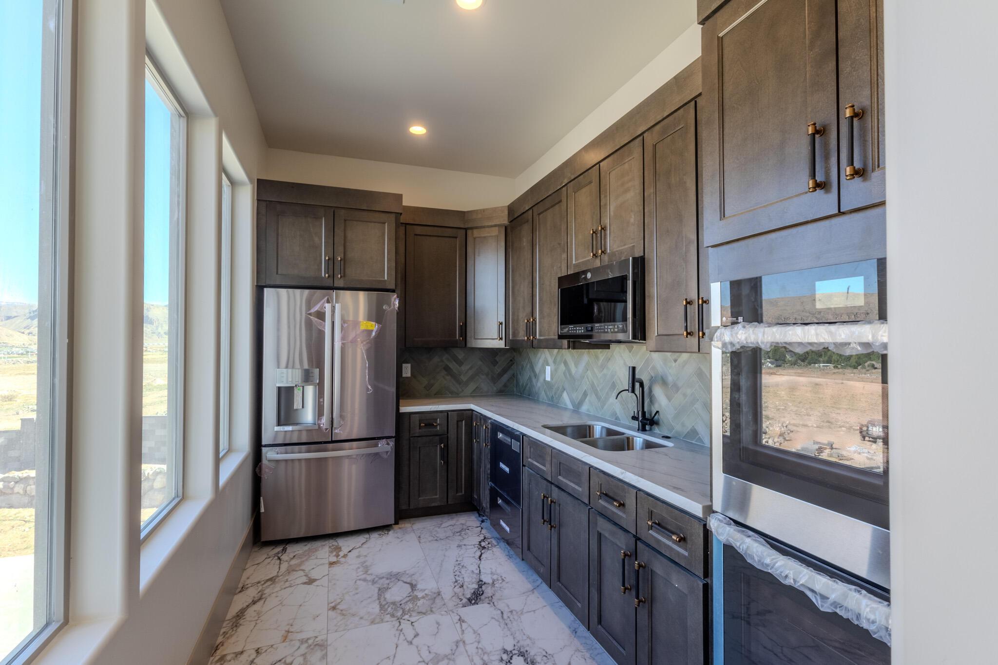 Modern kitchen featuring dark wood cabinetry with bronze hardware, stainless steel appliances, a herringbone tile backsplash, and a double basin sink with a matte black faucet