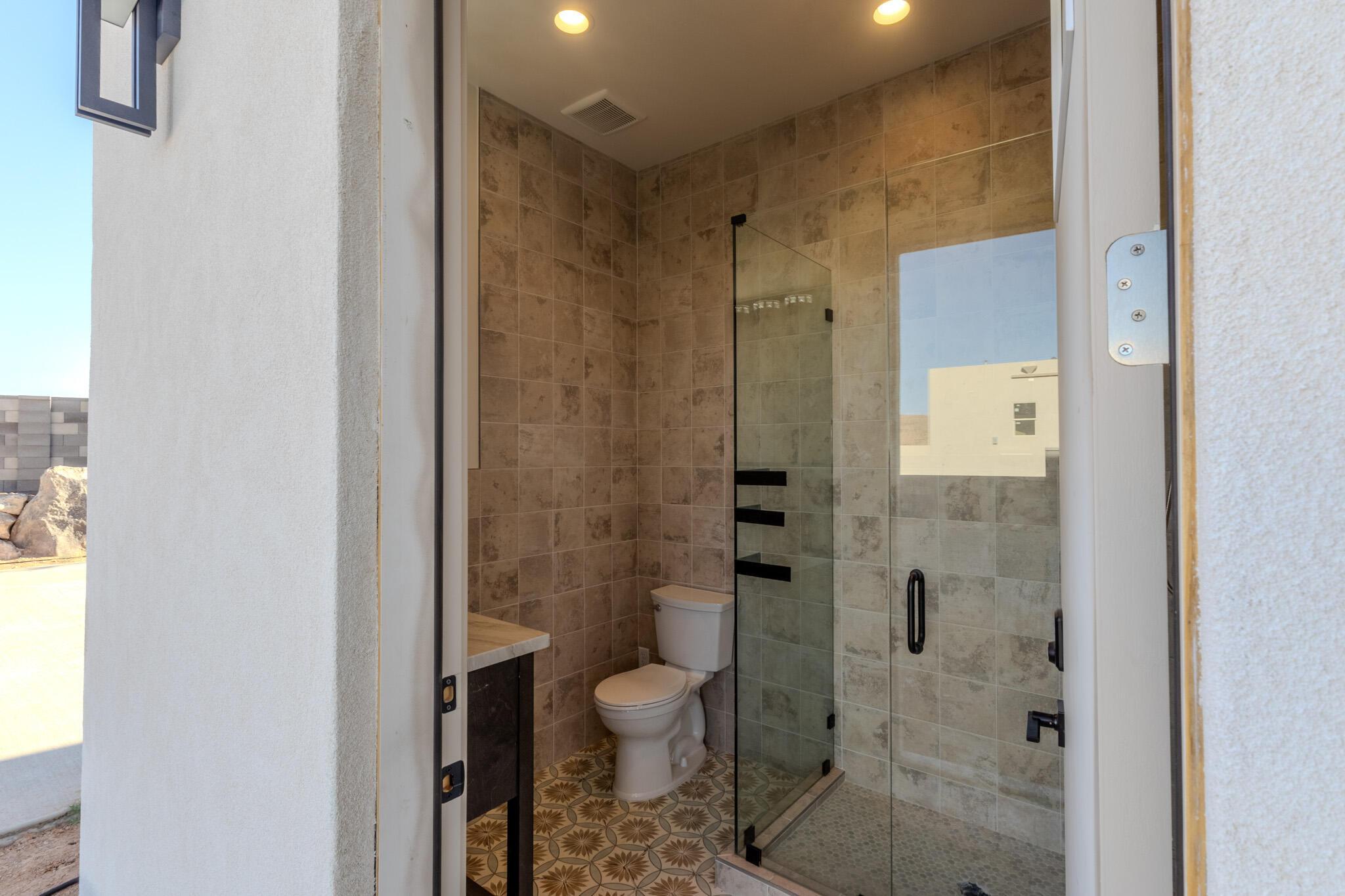Bathroom featuring a patterned tile floor, tiled shower surround, clear glass shower enclosure with matte black fixtures, and a vanity with a stone countertop