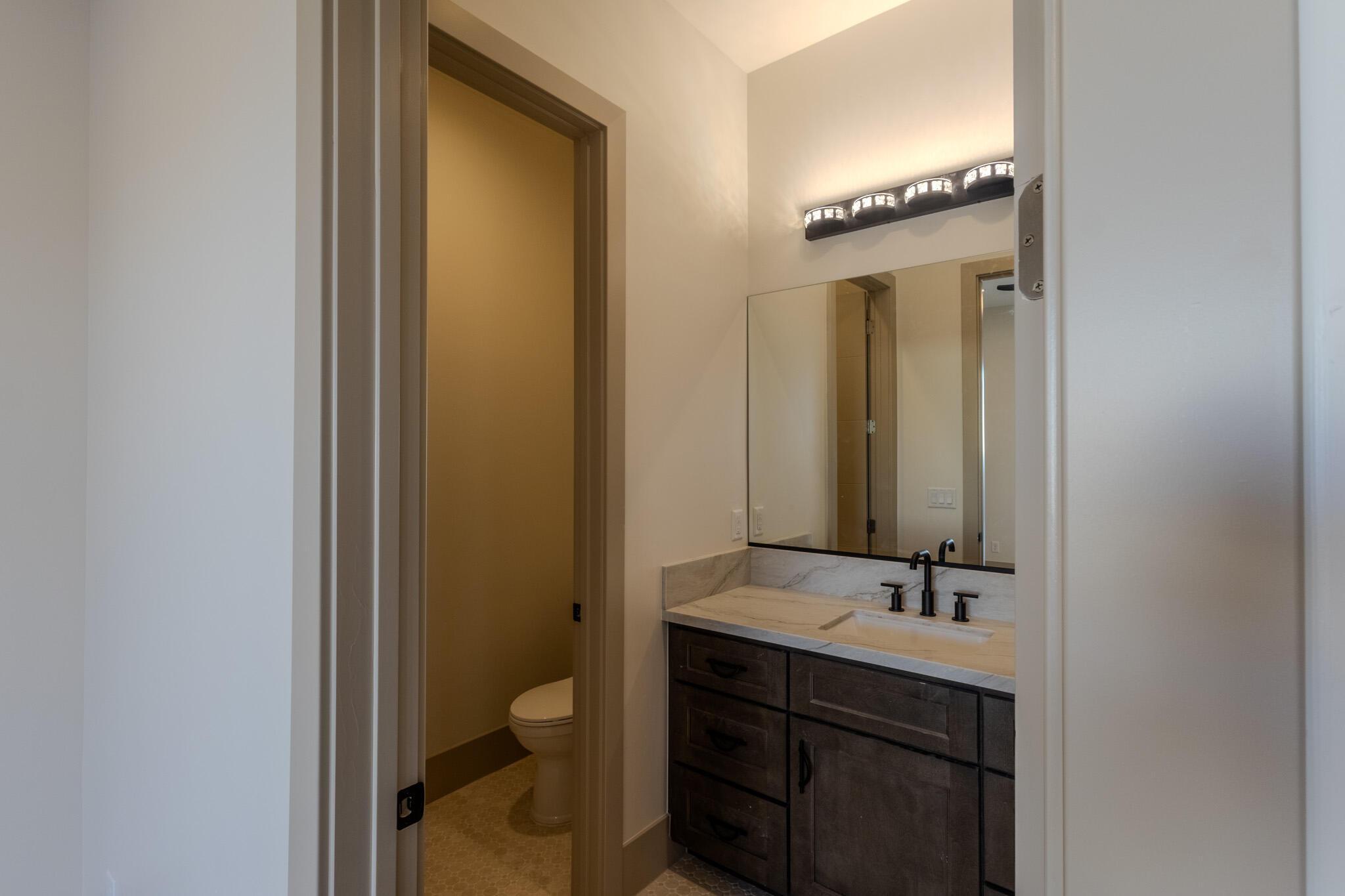 Vanity featuring a stone countertop, integrated rectangular sink, matte black hardware, and an overhead multi-bulb light fixture