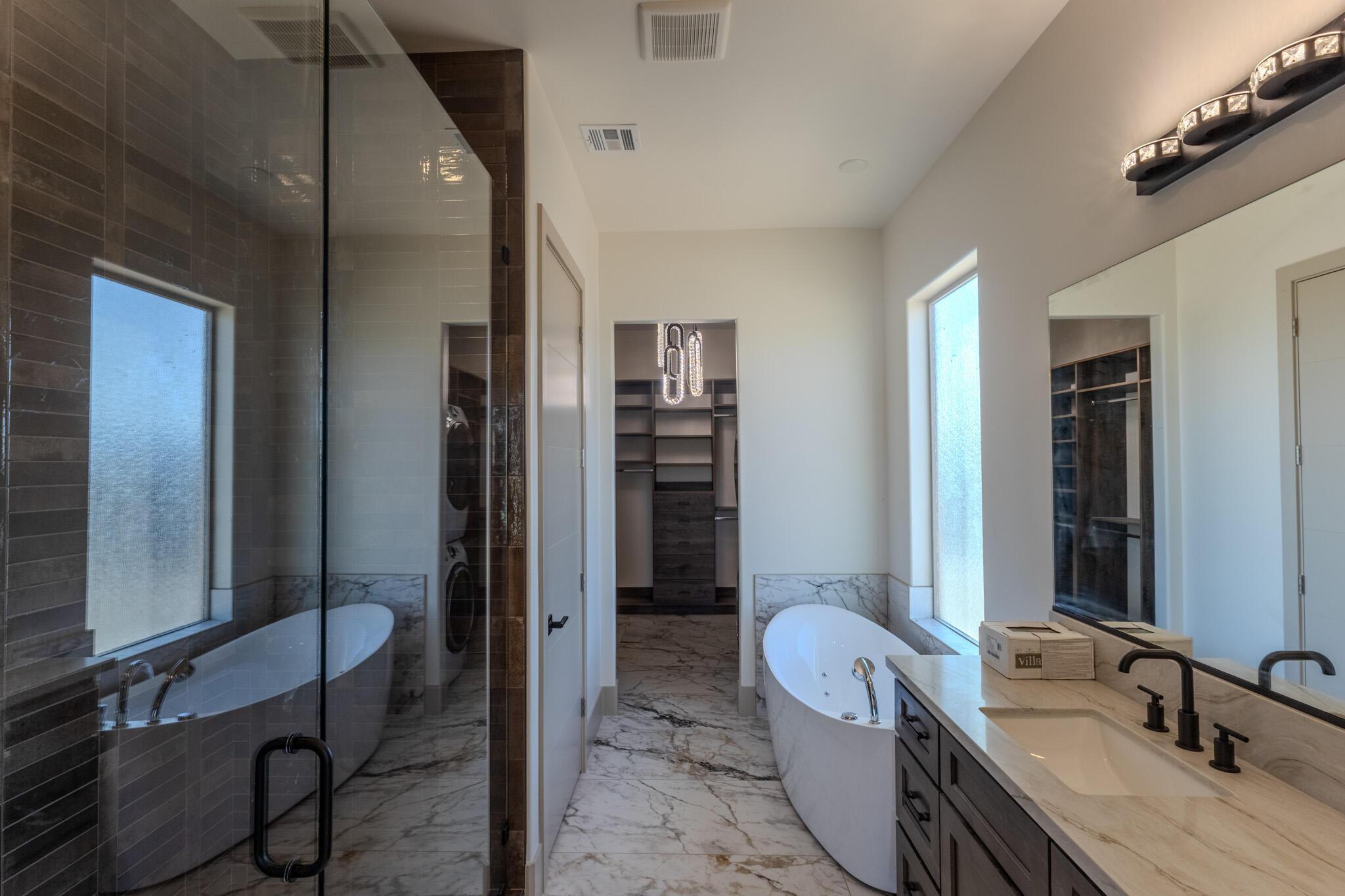 Luxurious bathroom featuring a freestanding soaking tub, a spacious glass-enclosed shower with tile surround, a dual vanity with a light-toned countertop, and rich wood-finish cabinetry