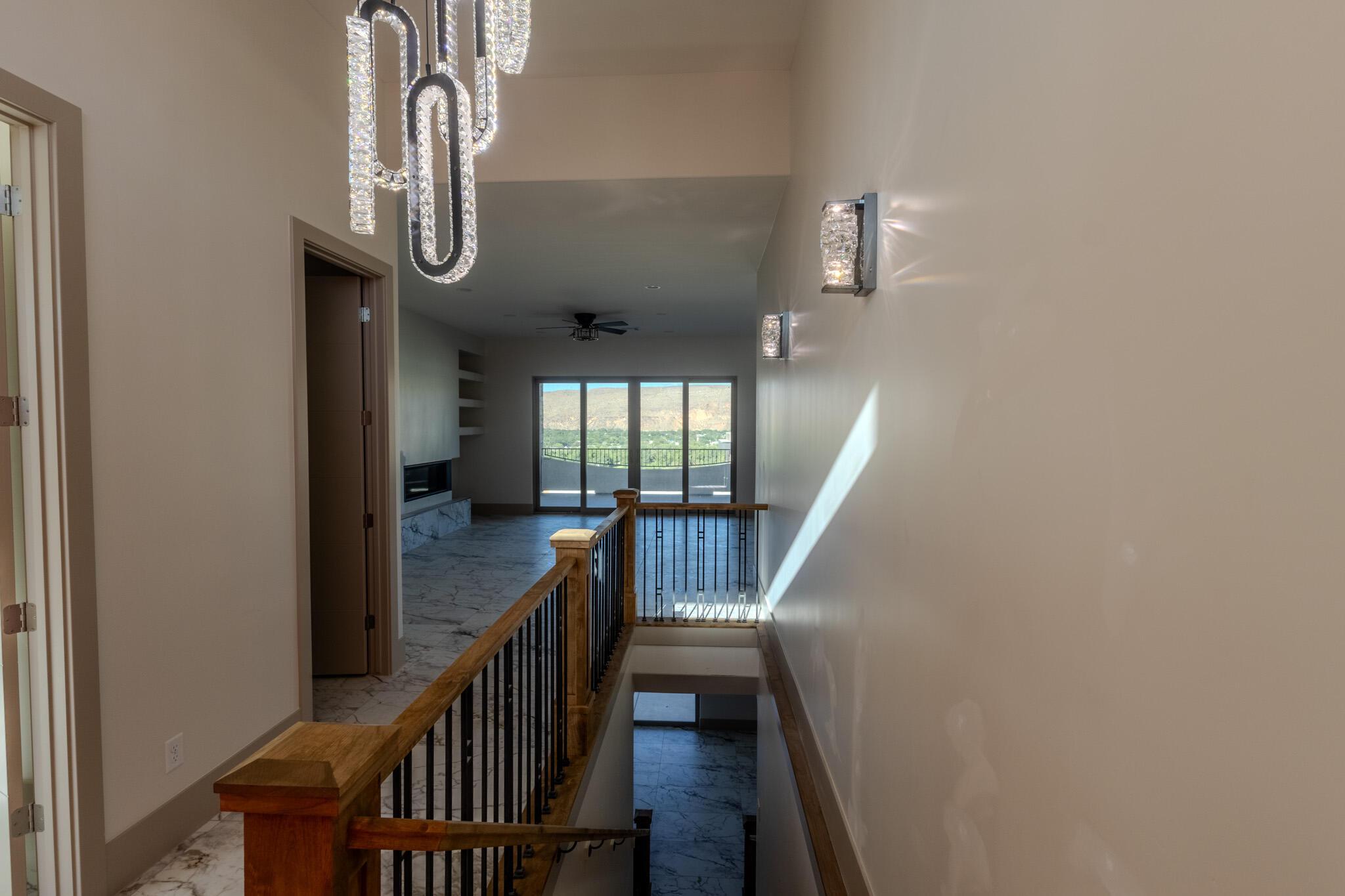 Stairwell featuring a wood handrail with black iron balusters, crystal chandelier, and wall sconces