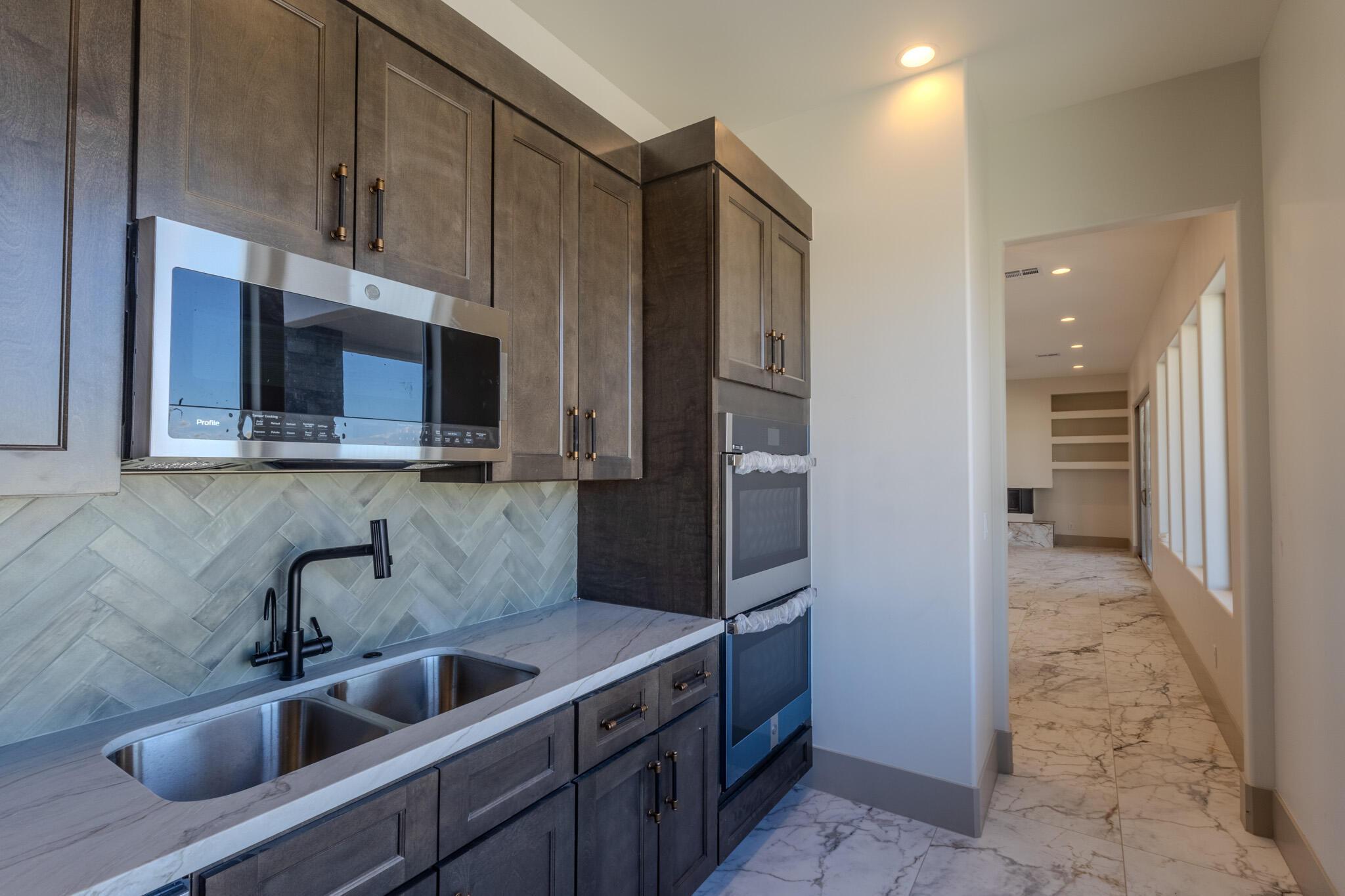 Contemporary kitchen area featuring stainless steel appliances, dark wood-finish cabinetry, a dual basin stainless steel sink with a matte black faucet, and a light-toned countertop