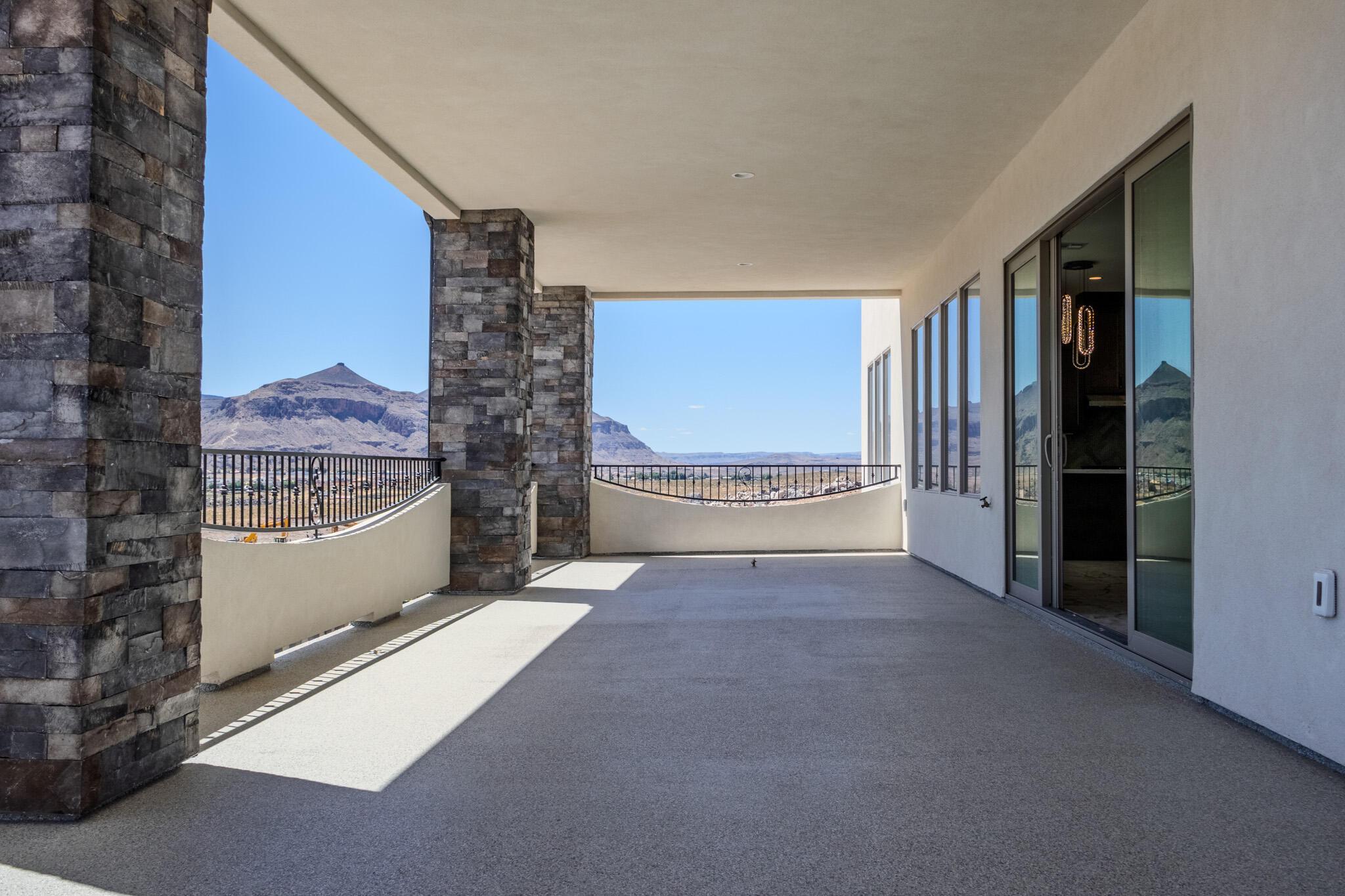 Spacious outdoor patio featuring stone-clad columns, a concrete surface, and a metal railing