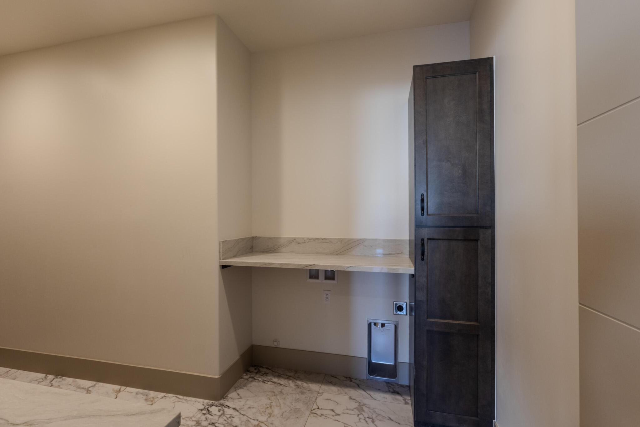 Laundry area featuring a built-in stone countertop, dark wood-finish cabinetry, and marble-look floor tiling