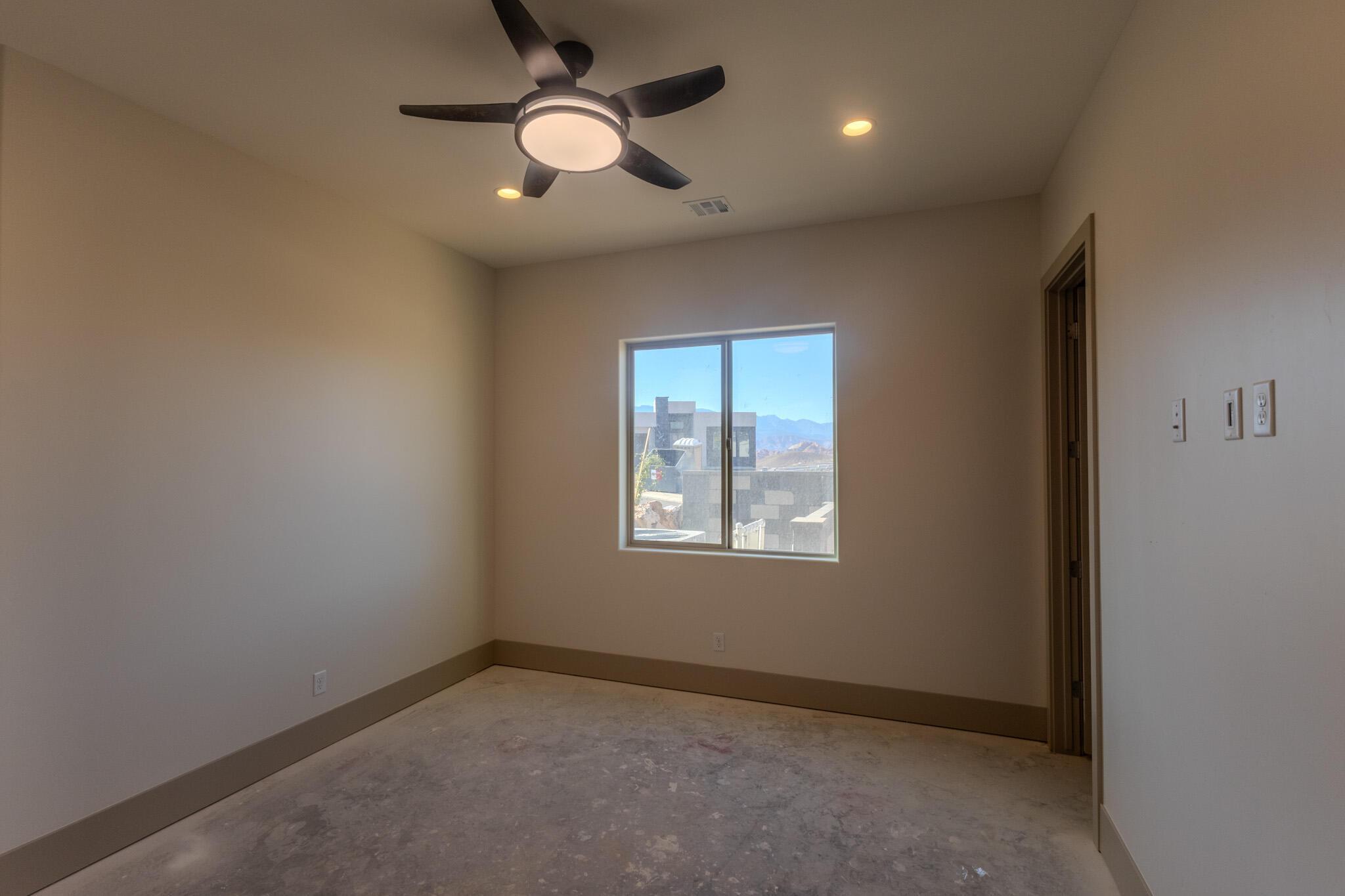 Spacious room featuring a modern ceiling fan with integrated lighting, recessed ceiling lights, a large window, and light-toned walls with contrasting baseboards