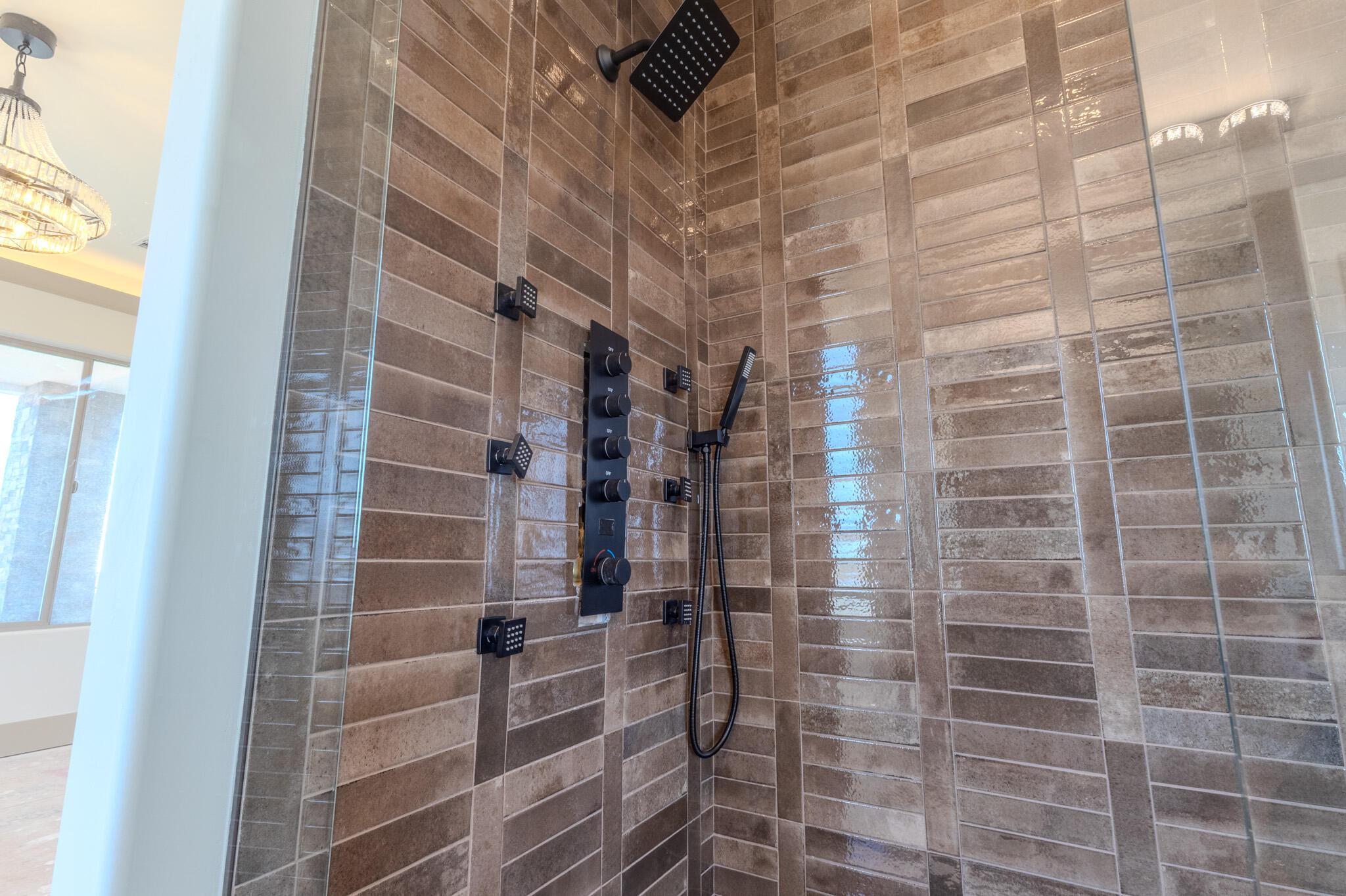 Tiled shower enclosure featuring a multi-function shower system with a rain showerhead, handheld sprayer, and body jets