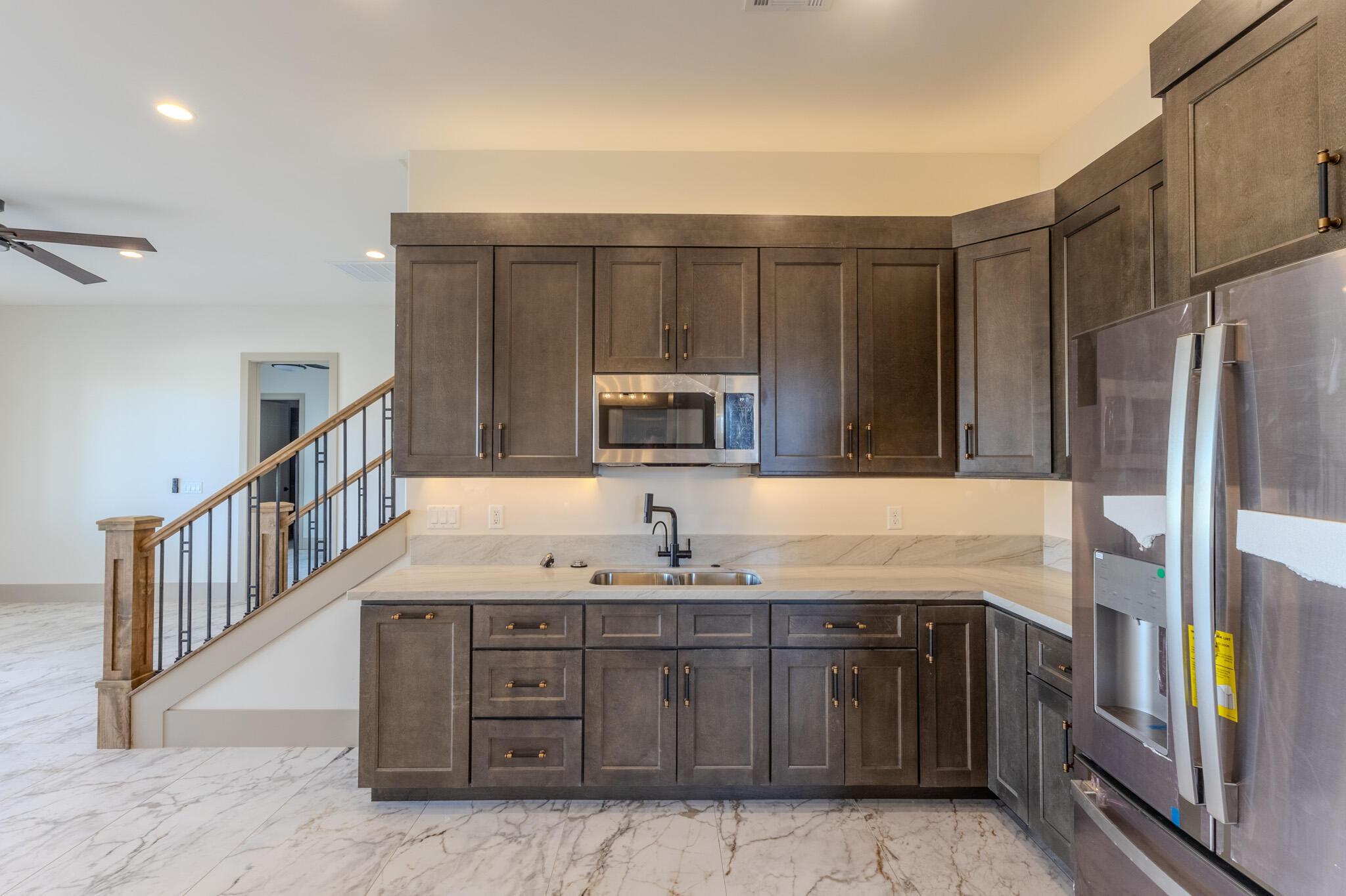 Kitchenette featuring dark wood cabinetry, white stone countertops, stainless steel microwave, and integrated refrigerator