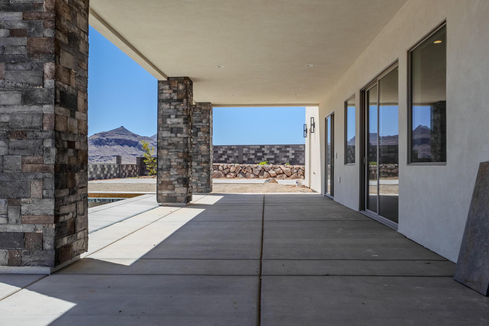 Expansive covered patio featuring stone-clad columns, concrete flooring, exterior wall sconces, and multiple sliding glass doors