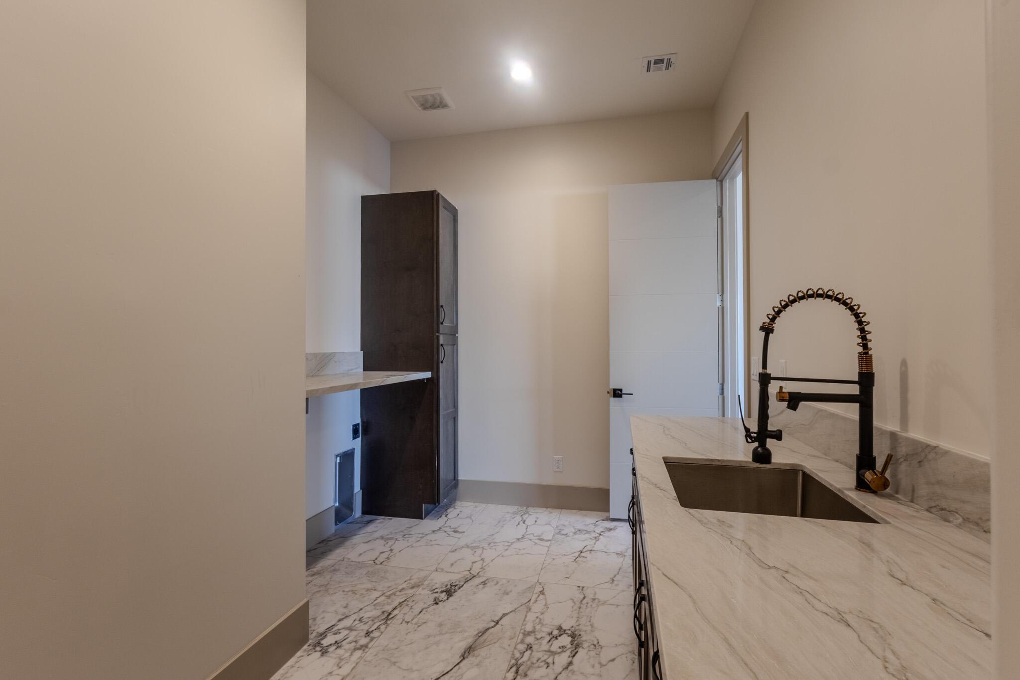 Utility room featuring high ceilings, marble-look flooring, stone countertops, a large utility sink with a matte black faucet, and tall built-in cabinetry