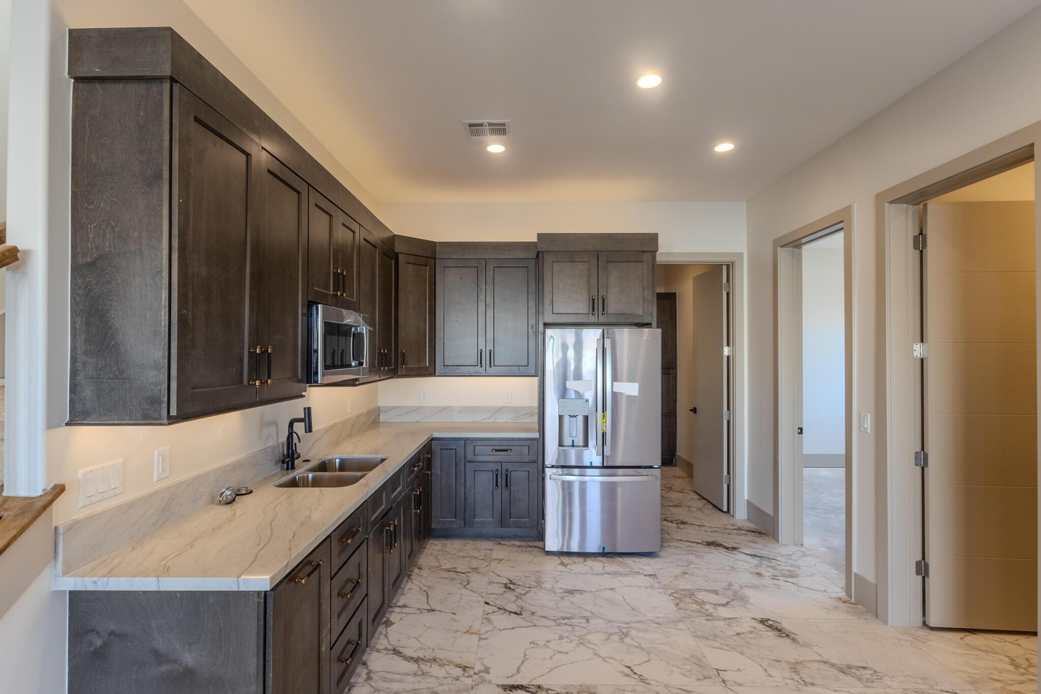 Kitchen featuring dark wood-finish cabinetry, light stone countertops, stainless steel appliances, and a double basin sink with a matte black faucet