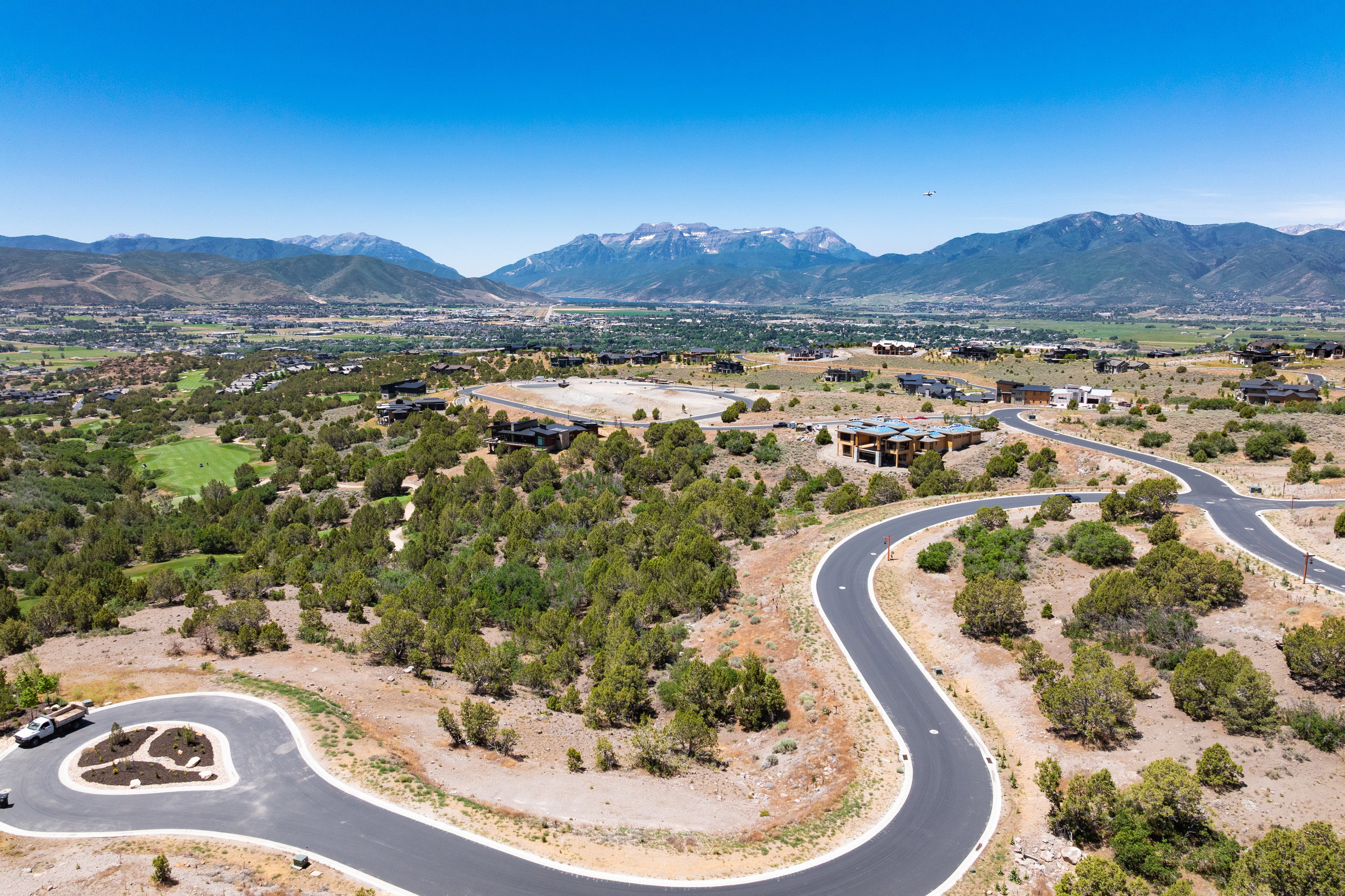 Winding paved roads through a natural landscape featuring mature trees and distant snow-capped mountains
