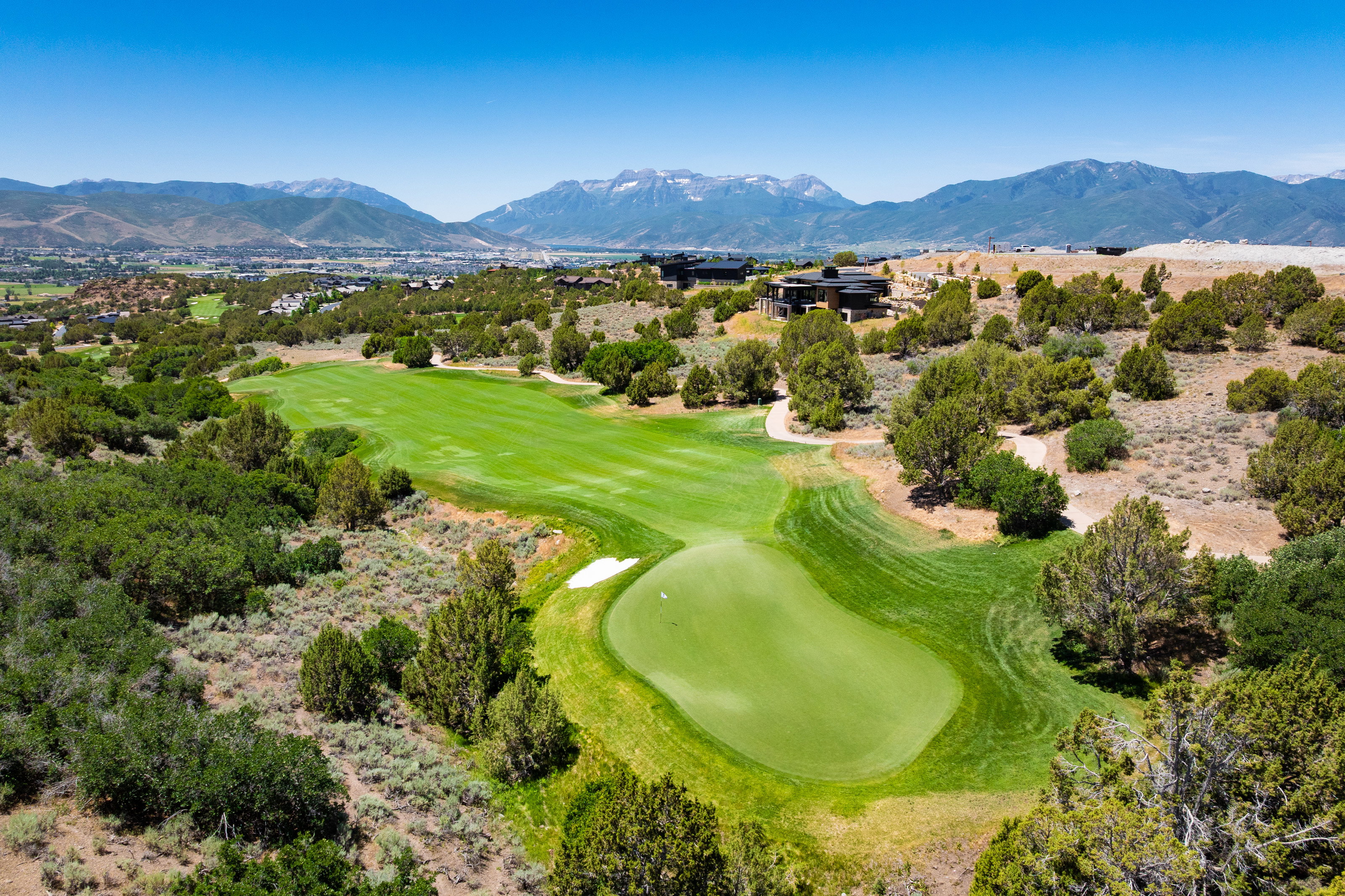 Expansive green golf course with a sand trap, surrounded by natural scrub brush and scattered trees