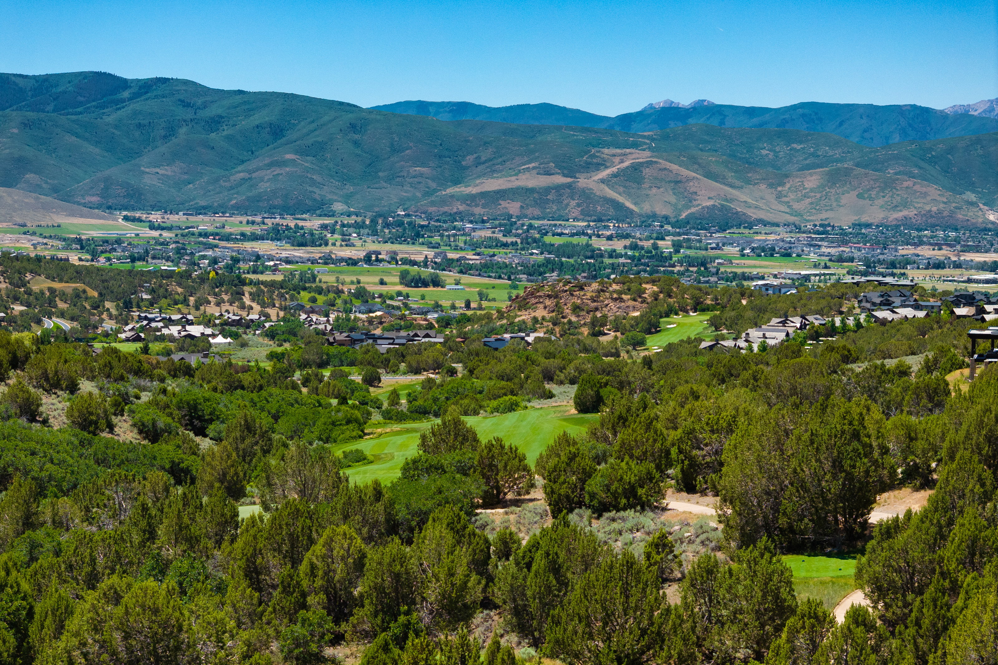 Expansive mountain valley scenery featuring distant residential areas, a lush green golf course, and abundant evergreen trees