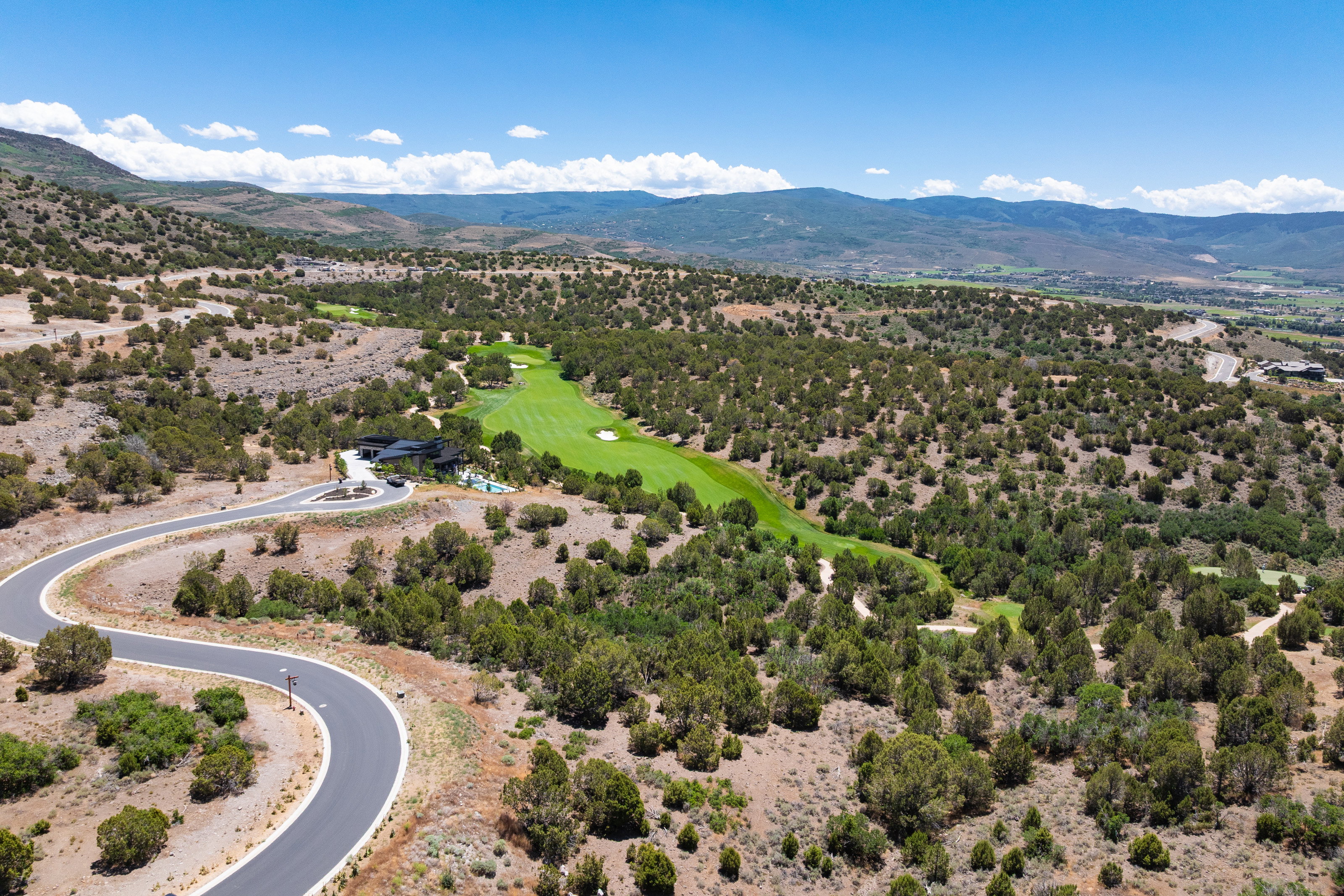 Expansive property featuring a winding paved road, a manicured golf course fairway, and distant mountain ranges