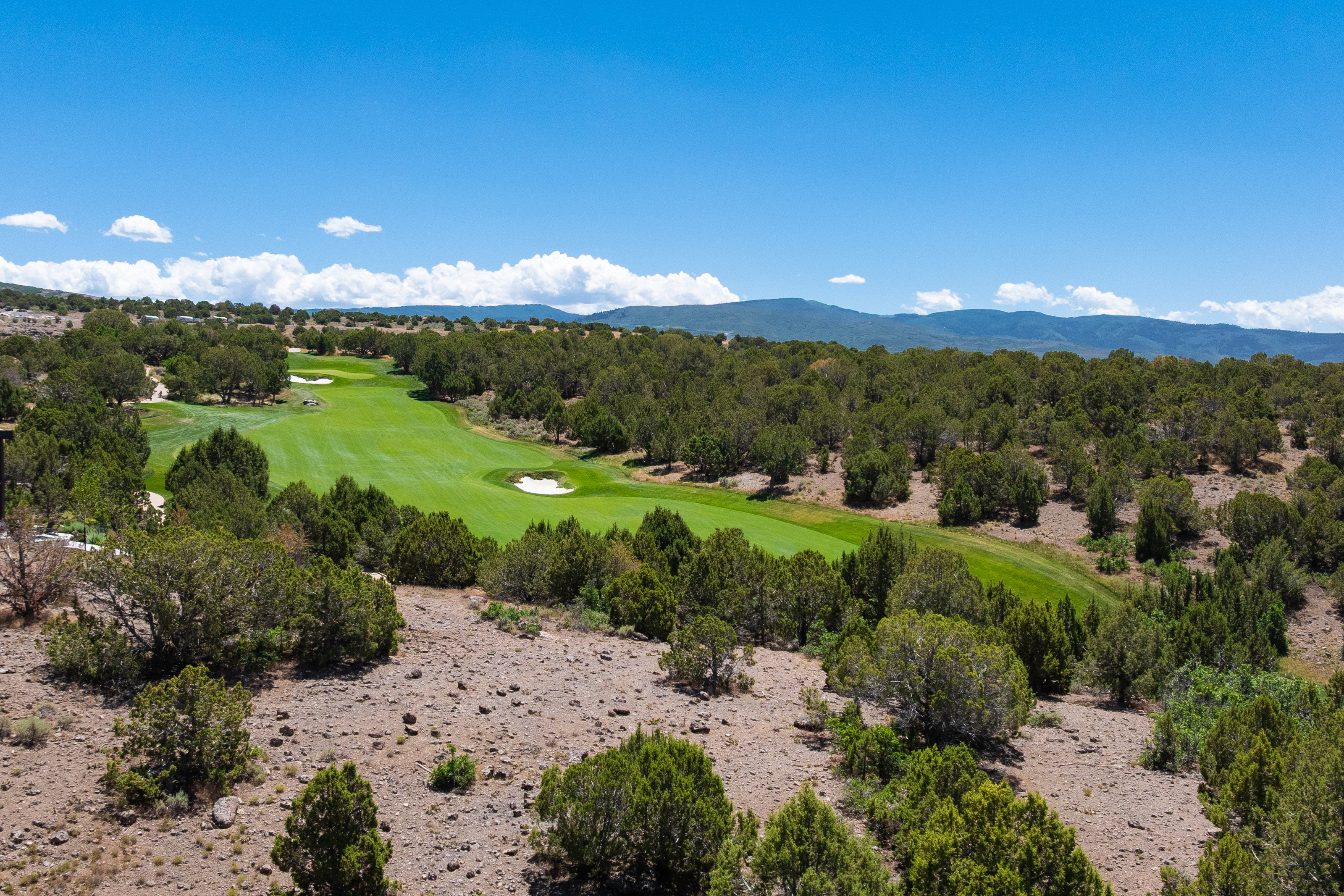 Expansive golf course frontage featuring manicured greens and sand traps, surrounded by native trees and rolling hills