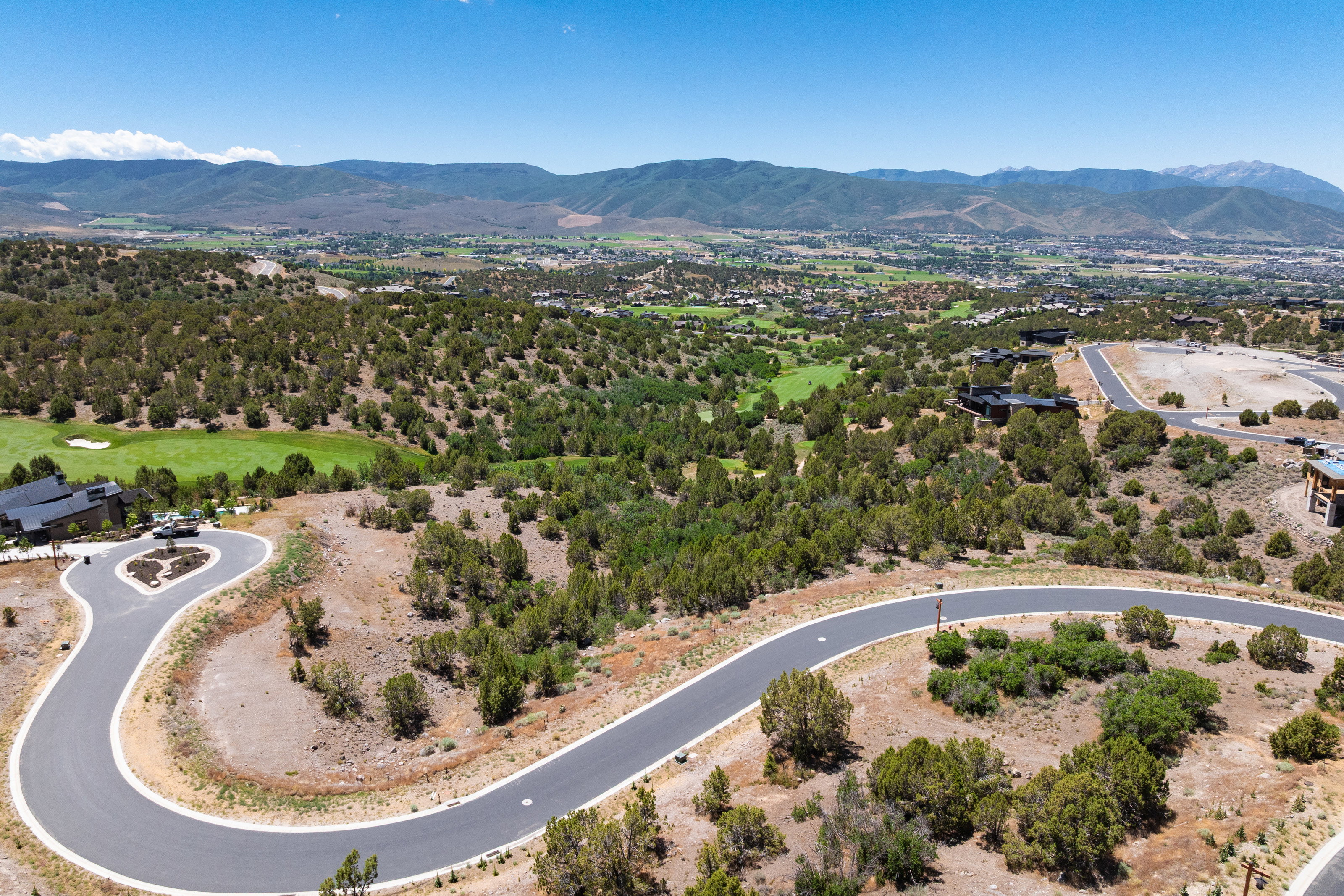 Curving paved roadway with white edge lining, surrounded by natural desert flora and distant mountain ranges