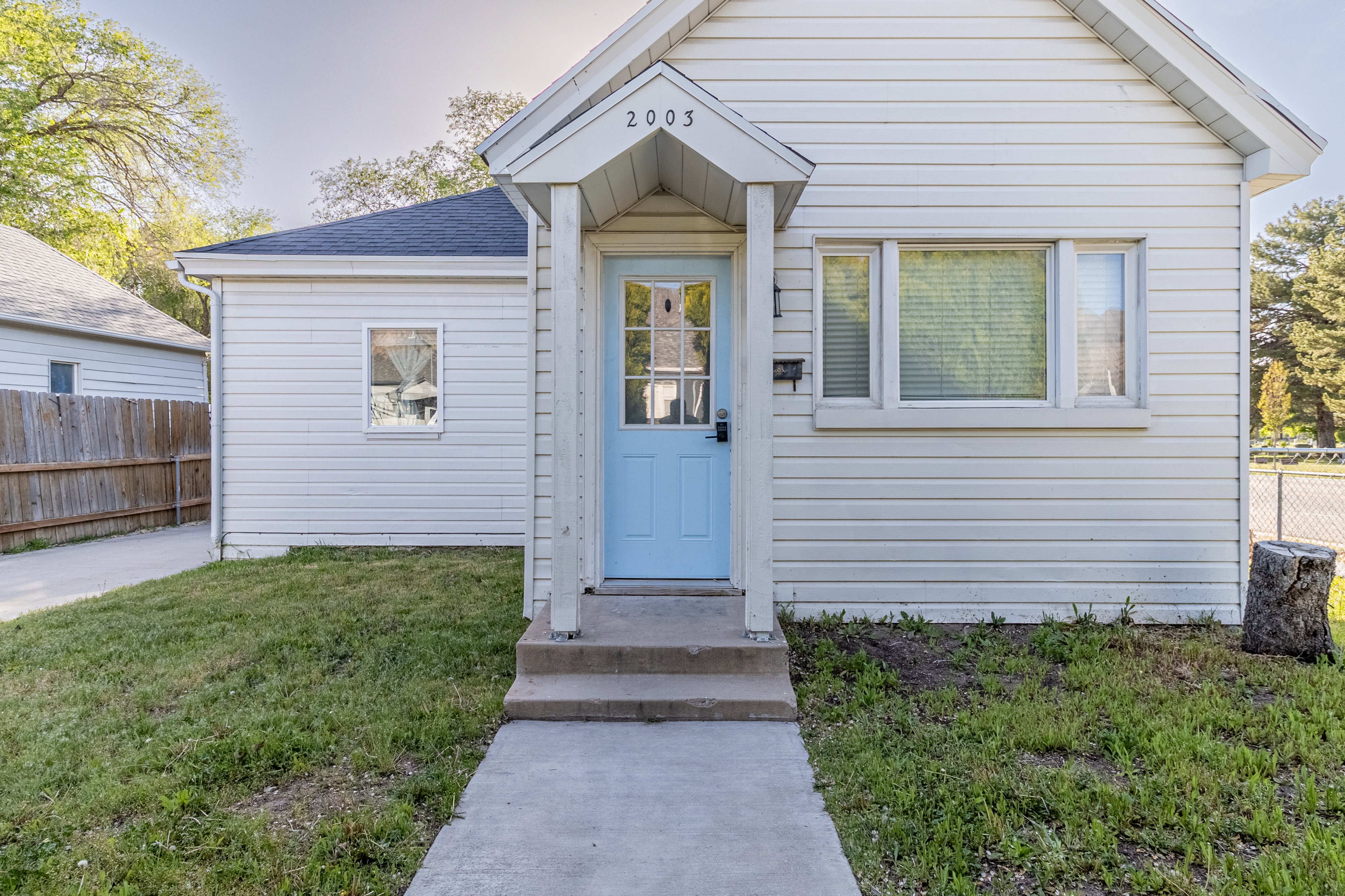 Front exterior featuring white horizontal siding, a light blue entry door with a glass panel, and a covered porch entry
