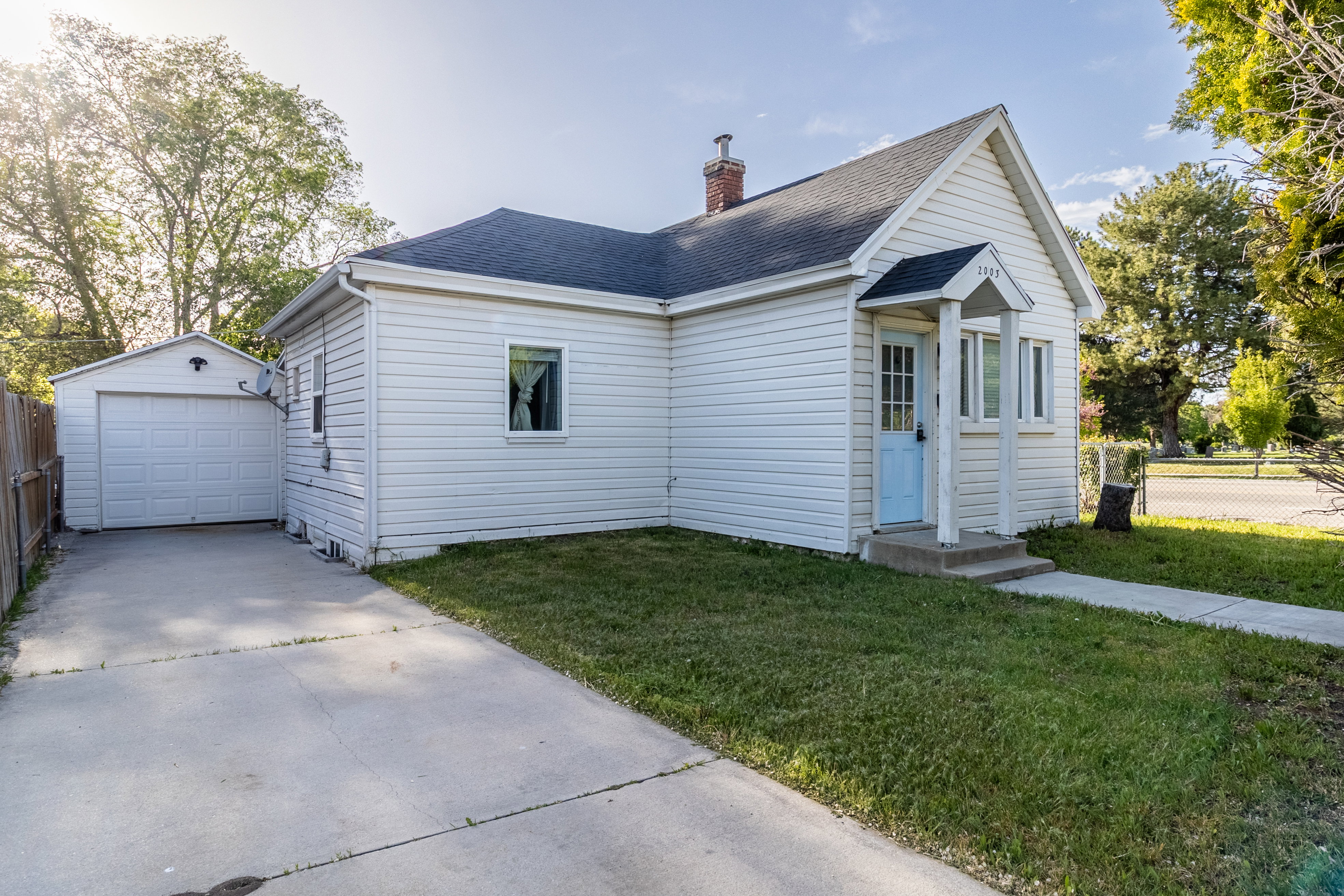 White siding exterior with a light blue front door, covered porch entry, and a paved driveway leading to a detached garage