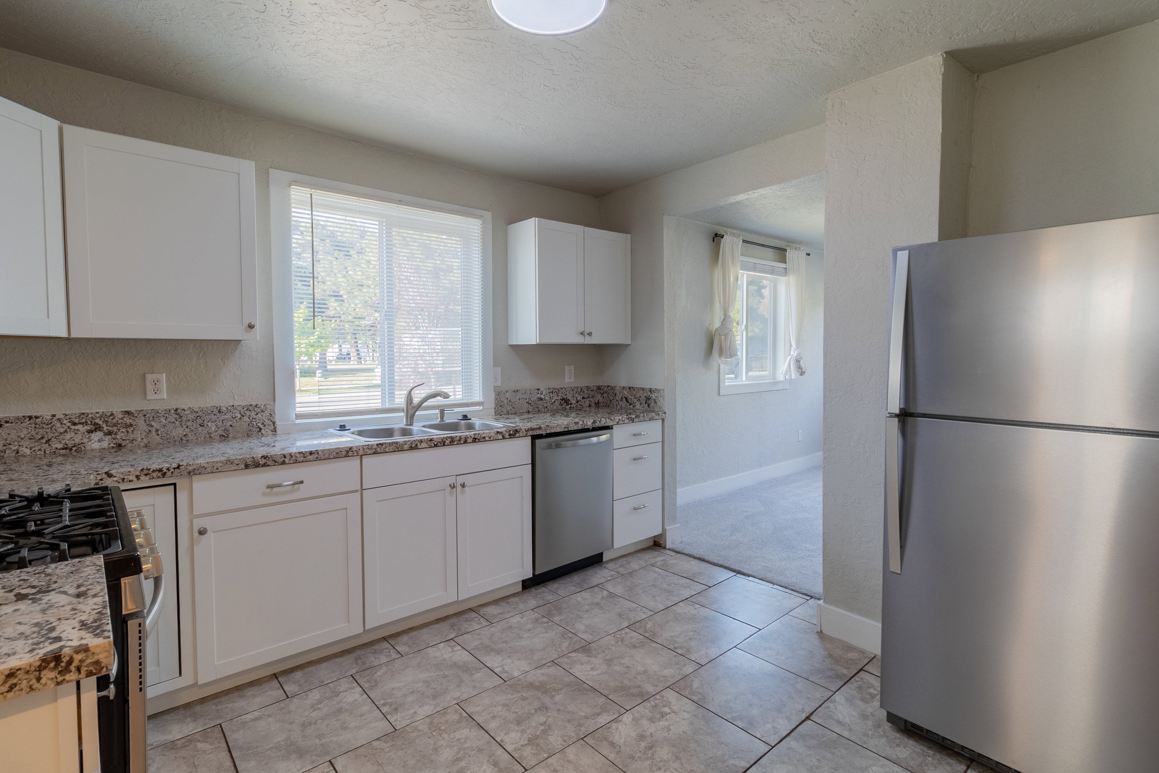 Spacious kitchen featuring white cabinetry, granite-style countertops, stainless steel appliances, a double basin sink with a chrome faucet, and tiled flooring
