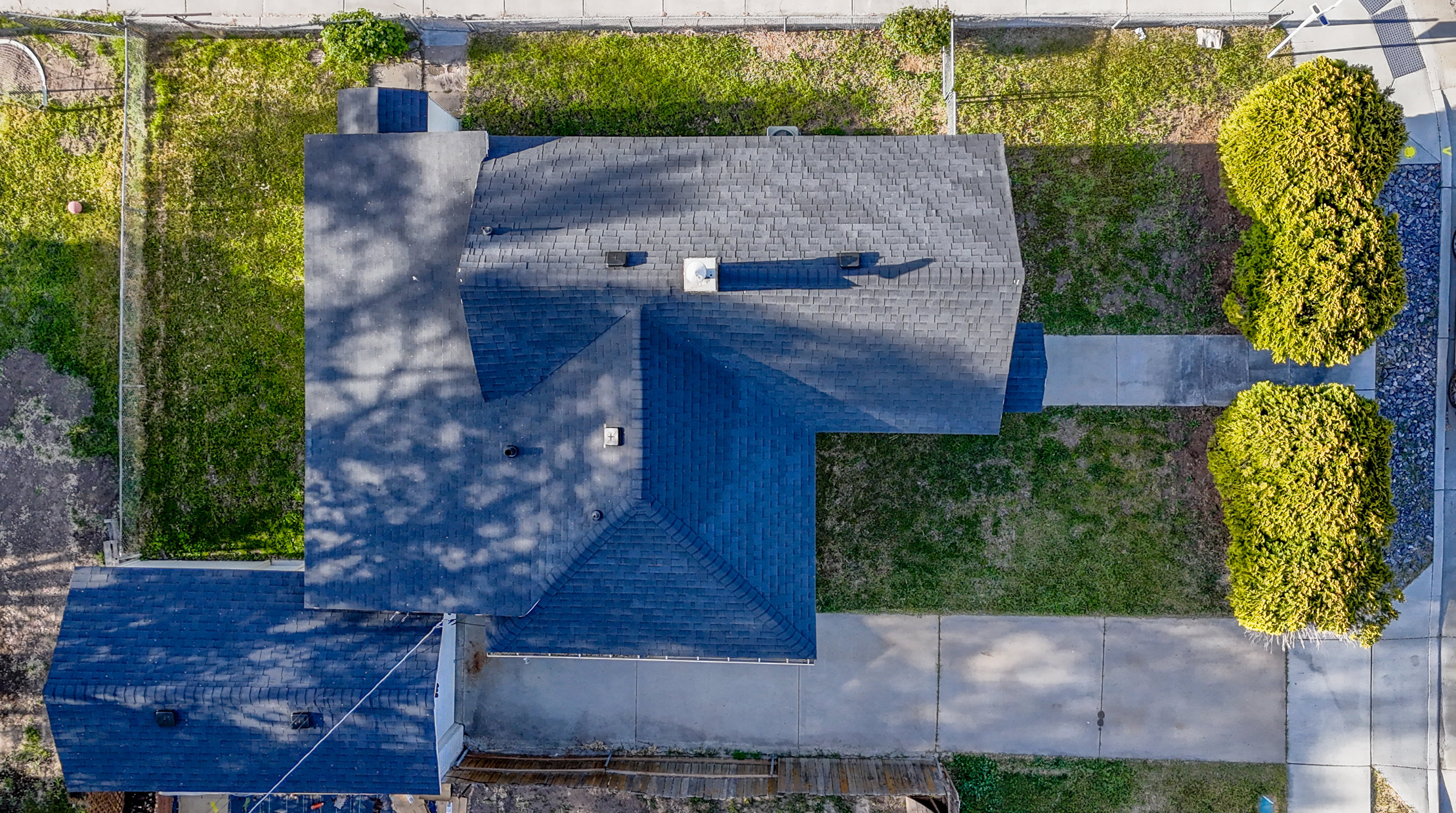 Property featuring a dark shingle roof, a concrete driveway, and a partially fenced backyard with a lawn