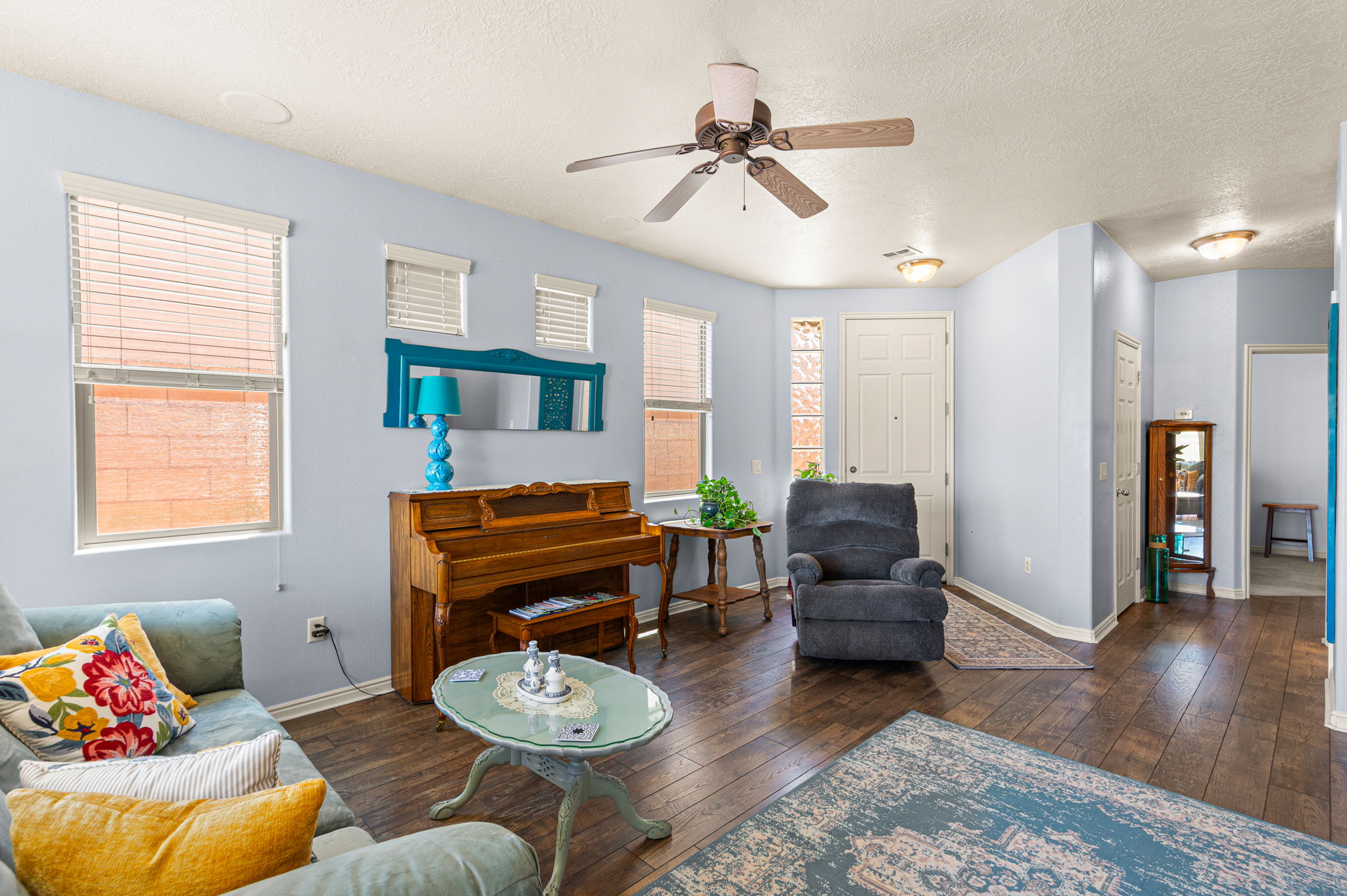 Spacious living area featuring wood-finish flooring, light blue walls, and a ceiling fan with integrated lighting