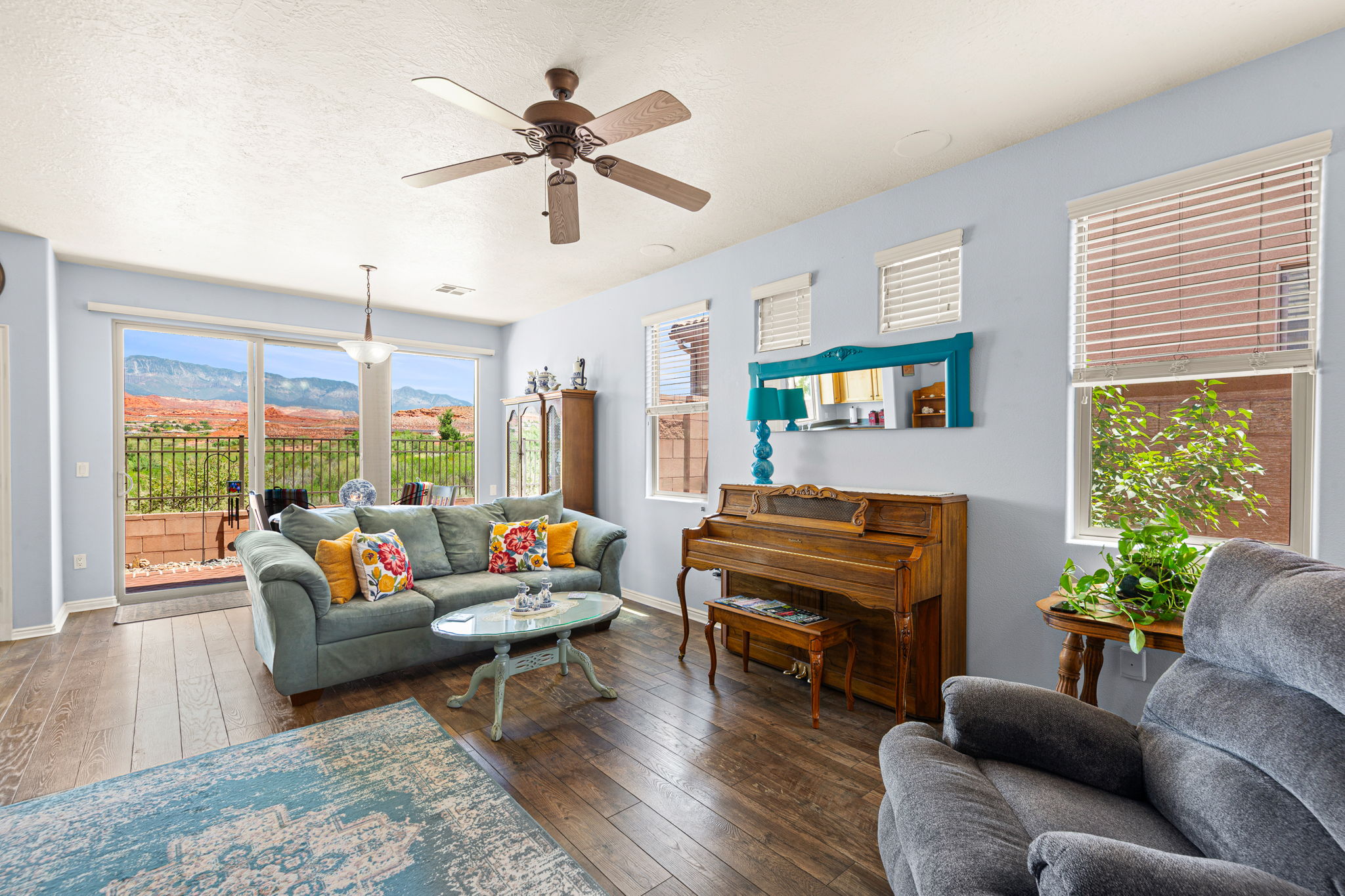 Spacious room featuring wood-finish flooring, a ceiling fan, and multiple windows with blinds