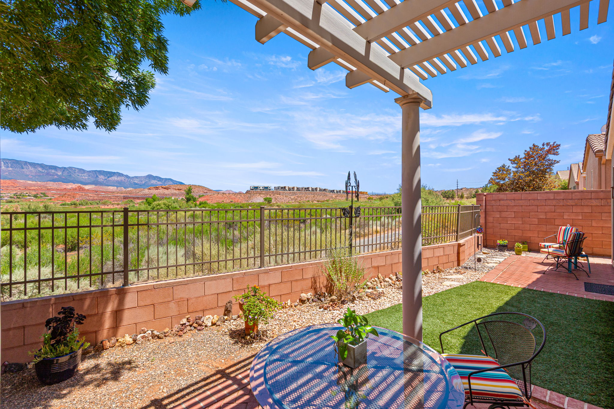 Outdoor patio featuring a white pergola, brick accent wall, and a combination of artificial turf and gravel landscaping