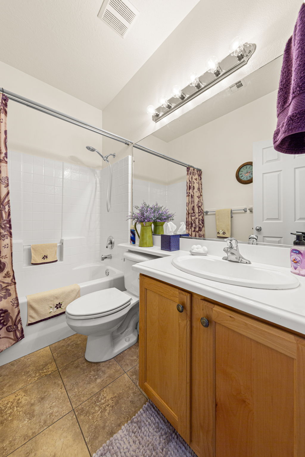 Bathroom featuring a light wood-finish vanity with a built-in sink, an extensive wall mirror, a full-size bathtub with shower, white tiled surround, and ceramic tile flooring
