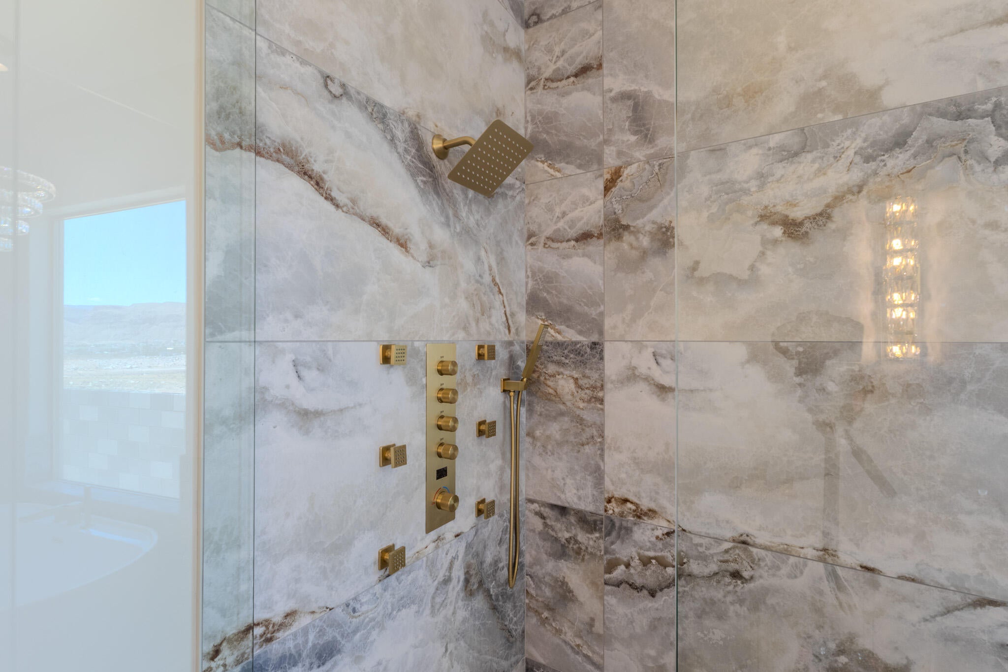 Walk-in shower featuring large format natural stone-look tile, a gold-finish rain shower head, a multi-function gold-finish body spray system, and a clear glass enclosure