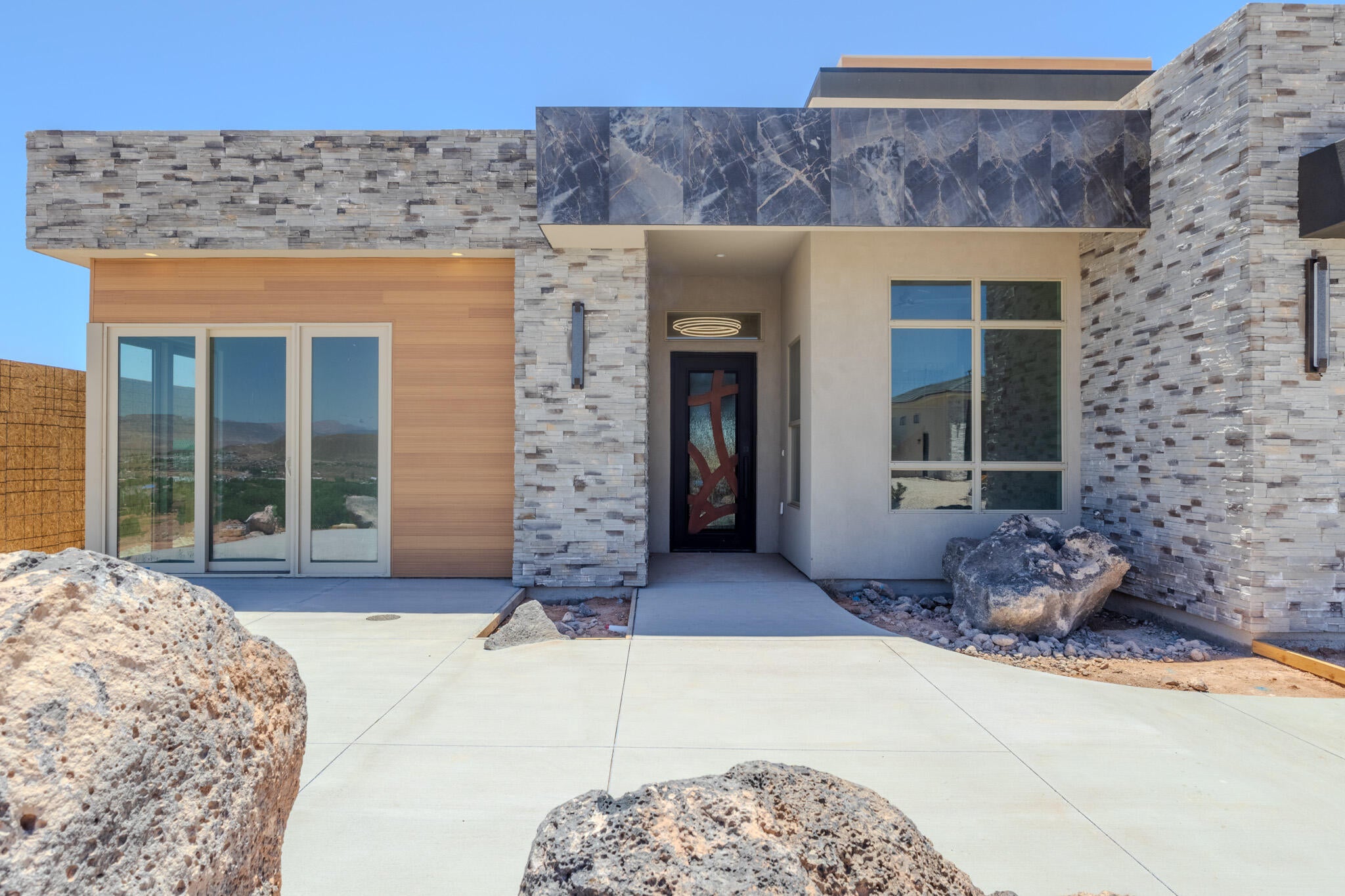 Contemporary facade featuring stacked stone accents, wood-finish paneling, and large format dark marble-look panels