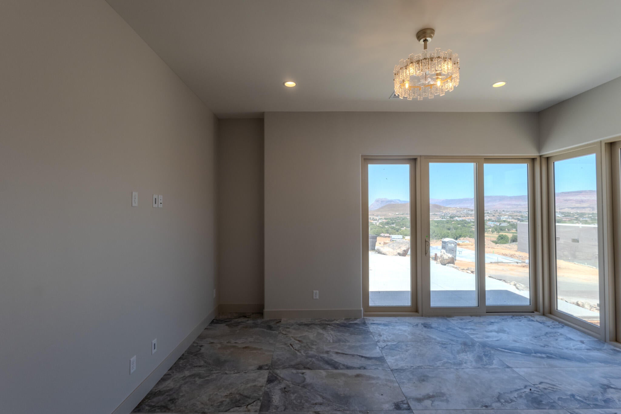 Spacious room featuring expansive glass sliding doors, tiled flooring, a contemporary chandelier, recessed lighting, and crisp neutral wall finishes