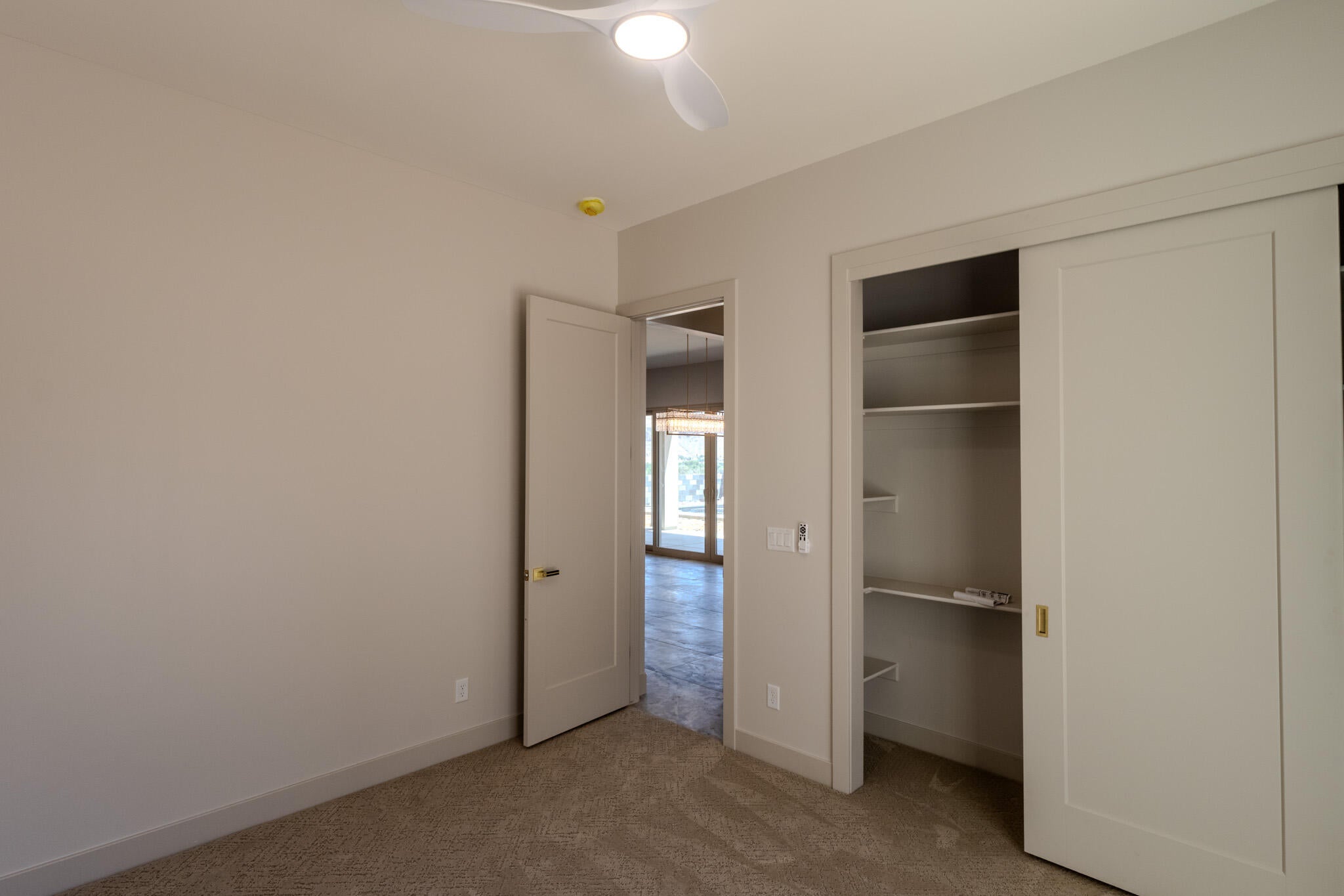 Carpeted interior space featuring a contemporary ceiling fan with integrated lighting, a solid core door, and a sliding door closet with built-in shelving